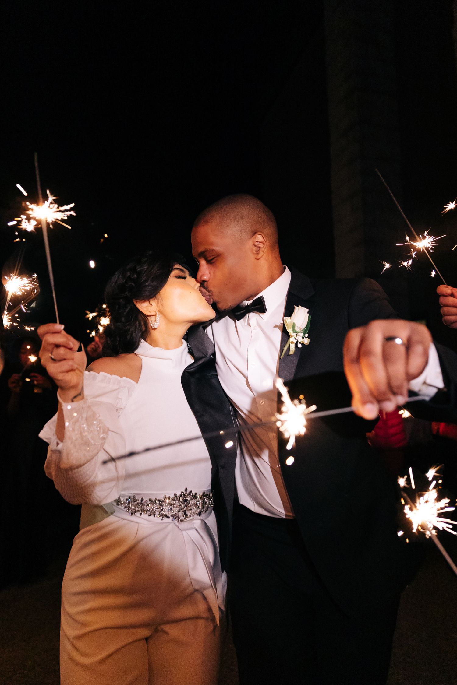 A romantic couple shares a tender moment while holding sparklers at a formal evening celebration.