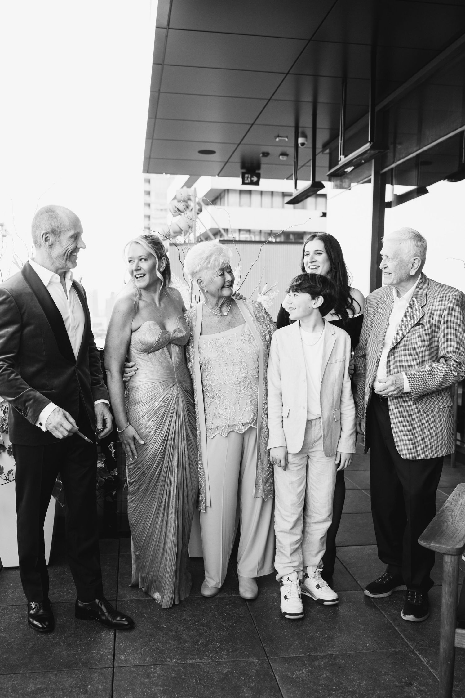 A group of five people in formal attire stand together at an outdoor event in black and white photography.