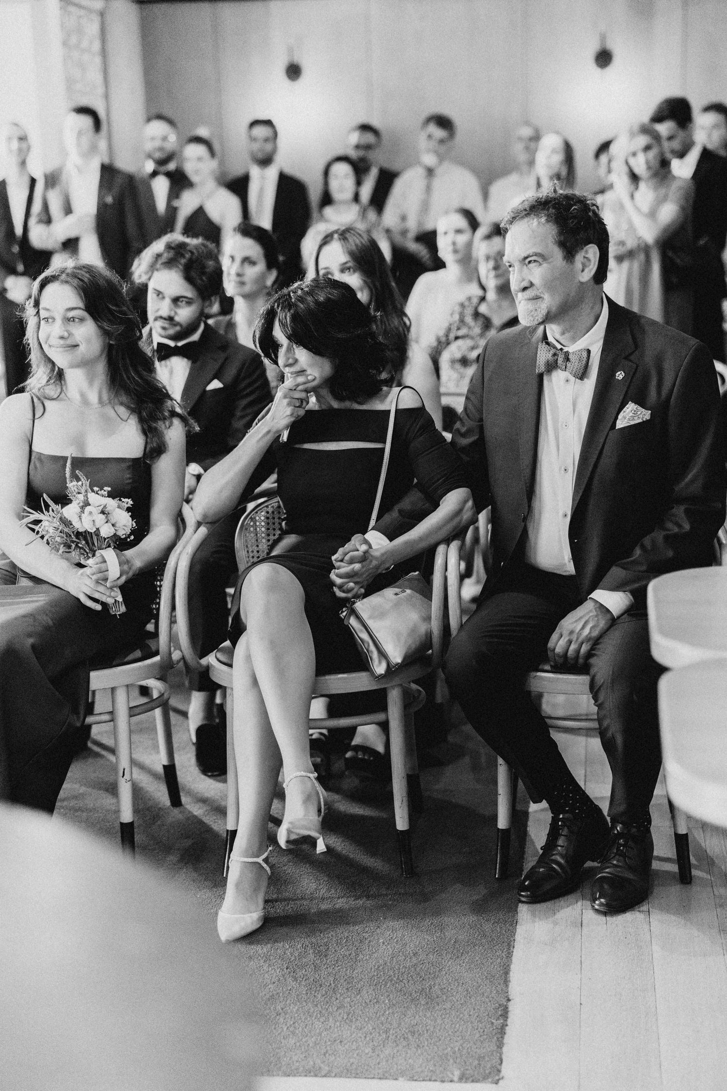 Wedding guests seated in formal attire watch a ceremony in an indoor venue.
