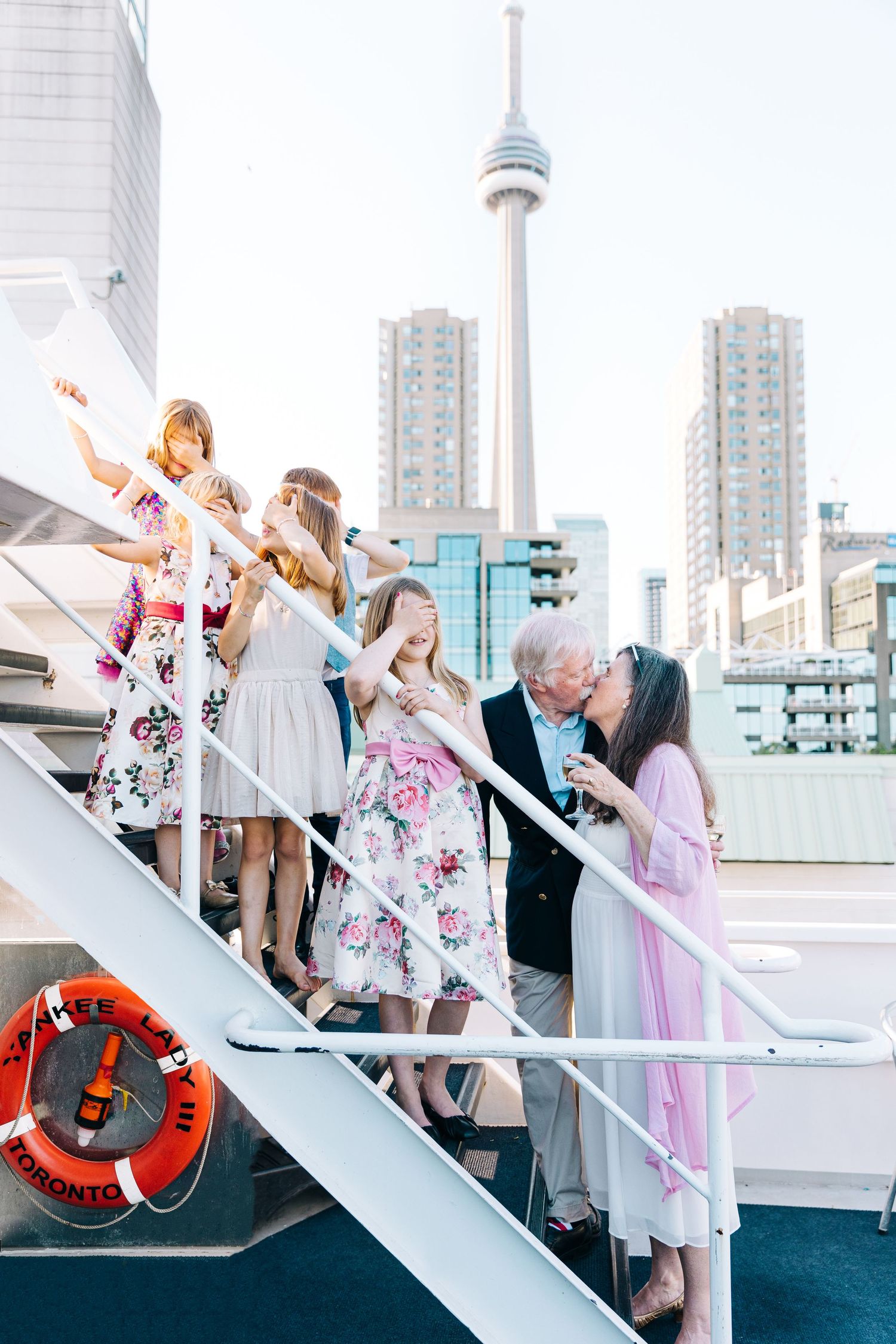People gather on a boat deck with Toronto's CN Tower and high-rise buildings in the background.