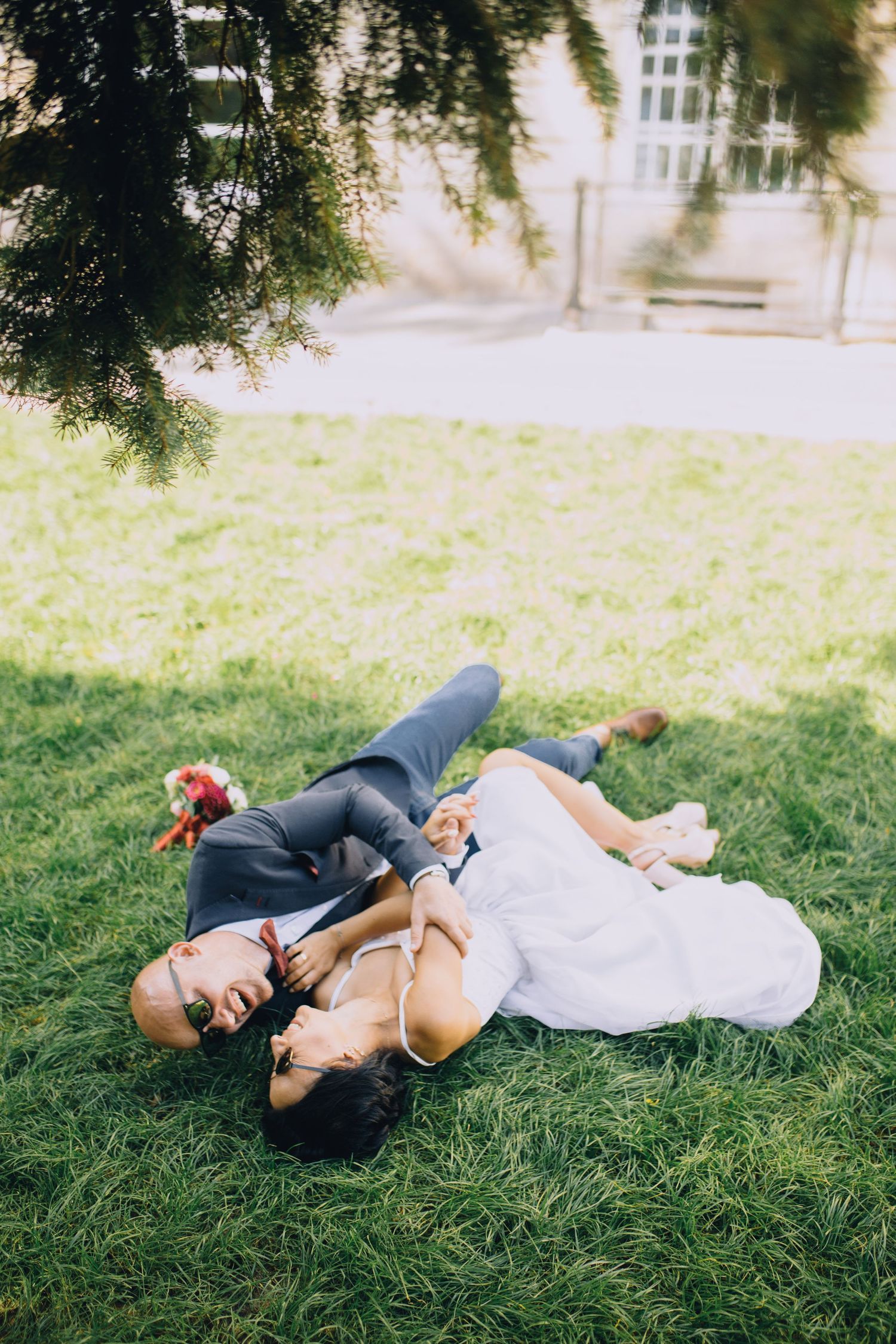 Two people lying down together on grass in casual attire during a sunny day in a park.
