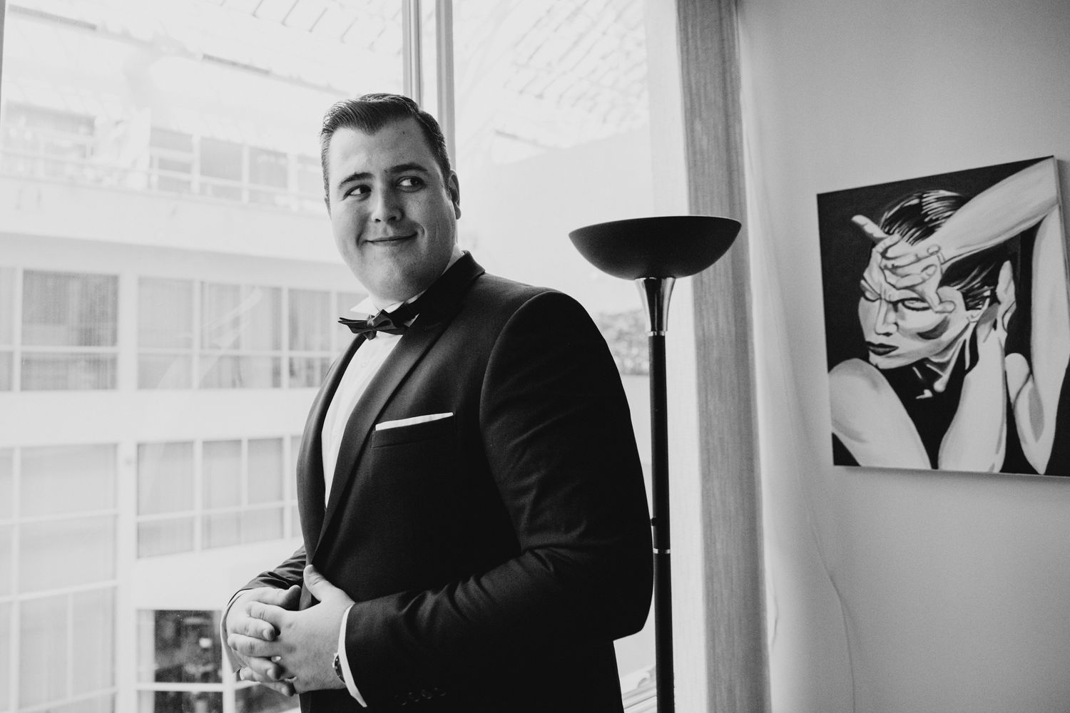 Man in black tuxedo and bowtie stands confidently in front of modern art.