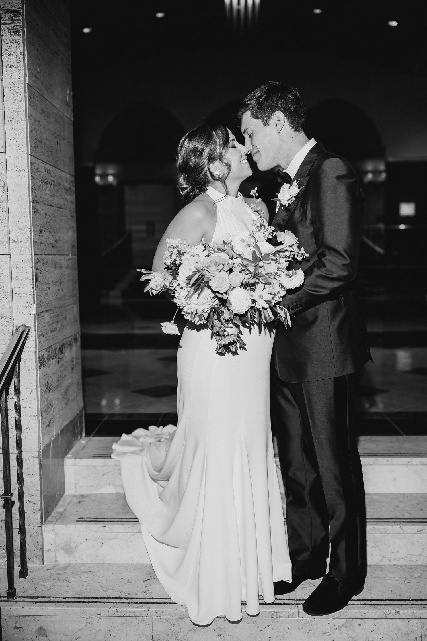 Black and white wedding photo of bride in elegant white gown holding floral bouquet sharing intimate moment with groom.