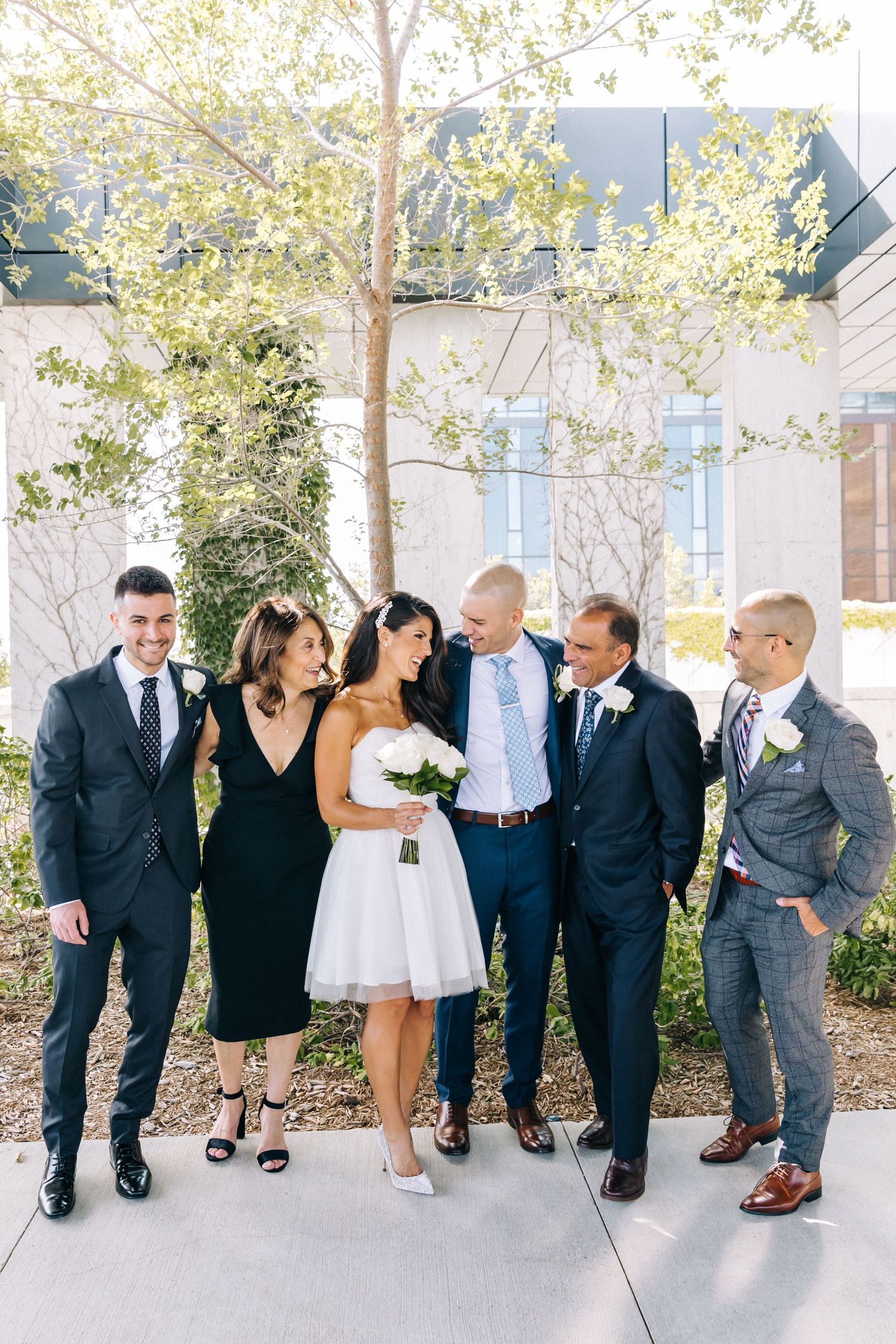 Wedding party in formal attire posing together outdoors under blooming trees.