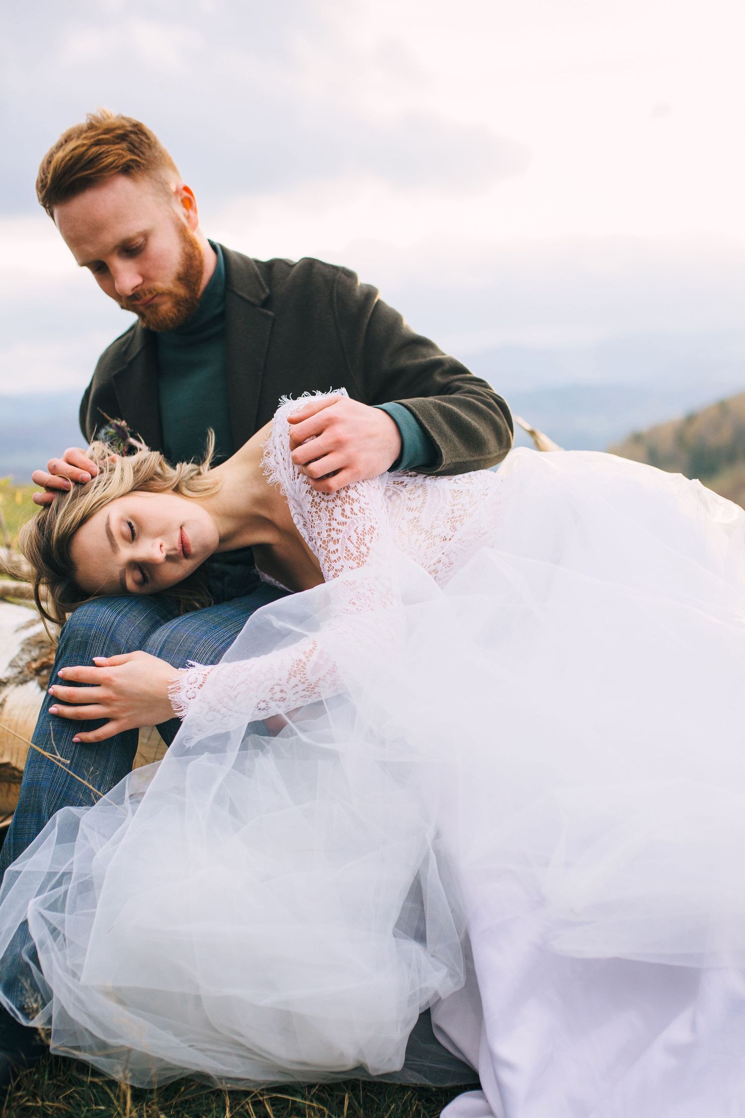 A couple in wedding attire share an intimate moment outdoors against a mountain backdrop with soft lighting.
