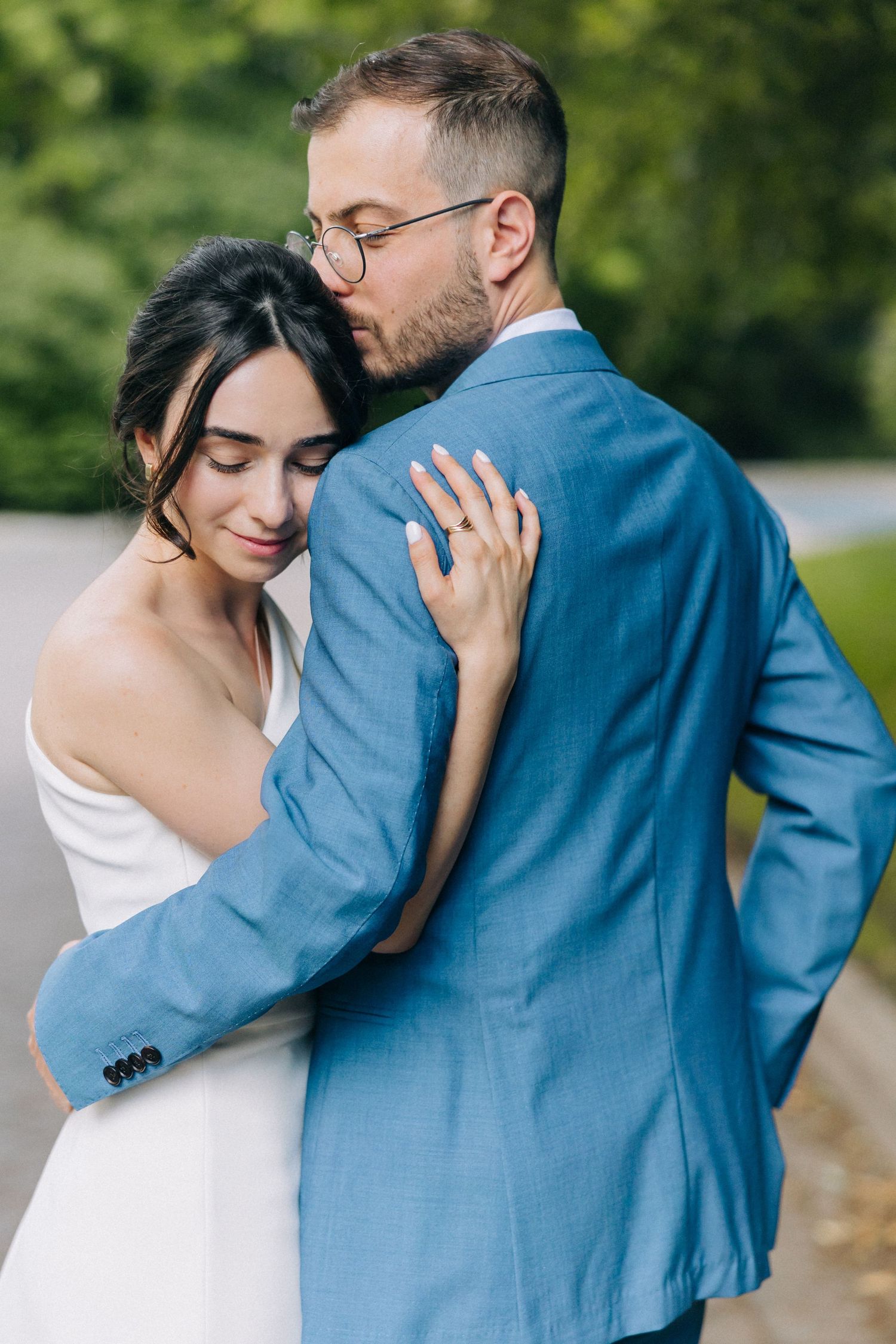 A romantic embrace between newlyweds, with the bride in white and groom in a blue suit sharing an intimate moment outdoors.
