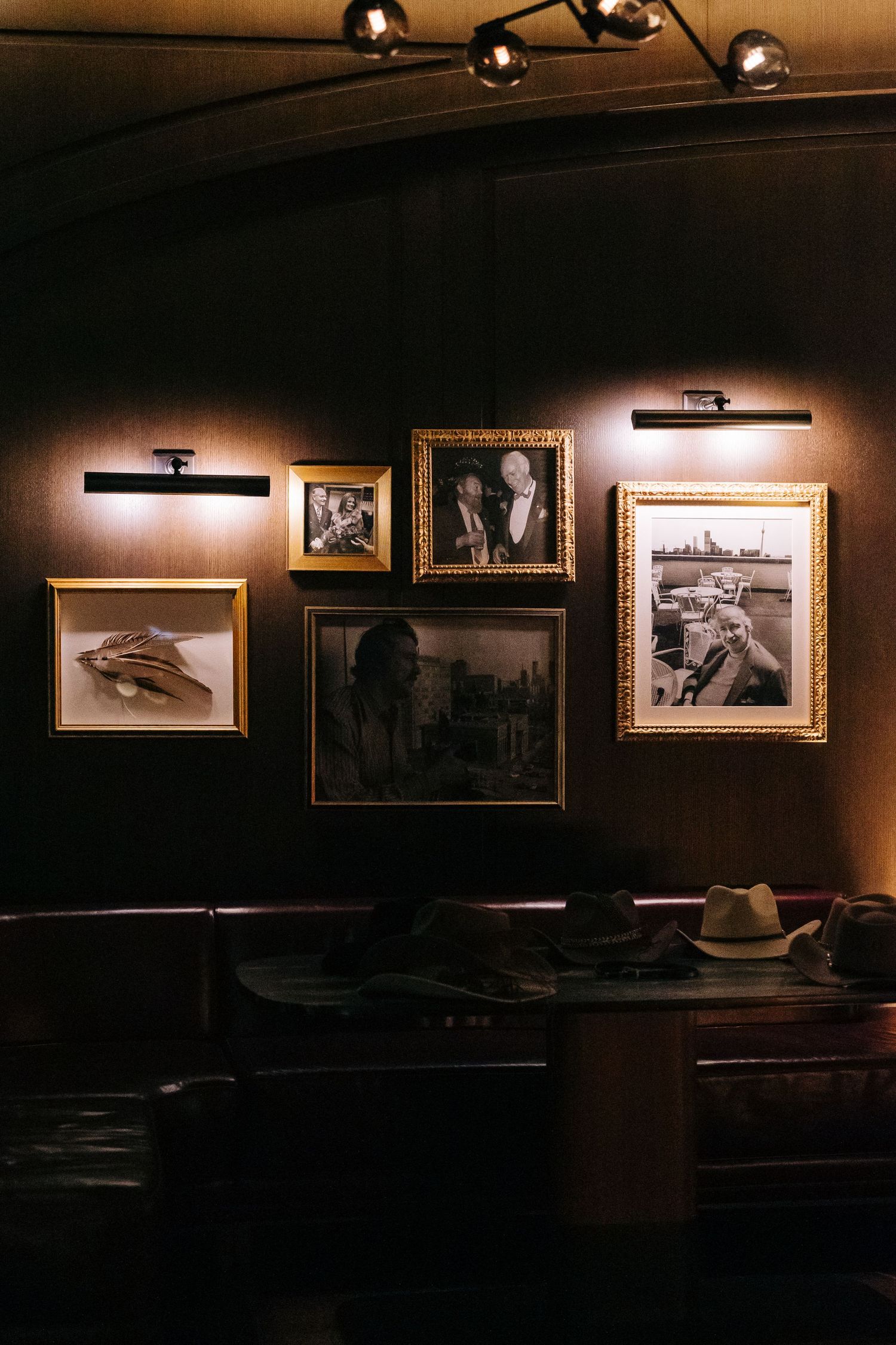 Dimly lit wall with vintage photographs and artwork in gold frames.