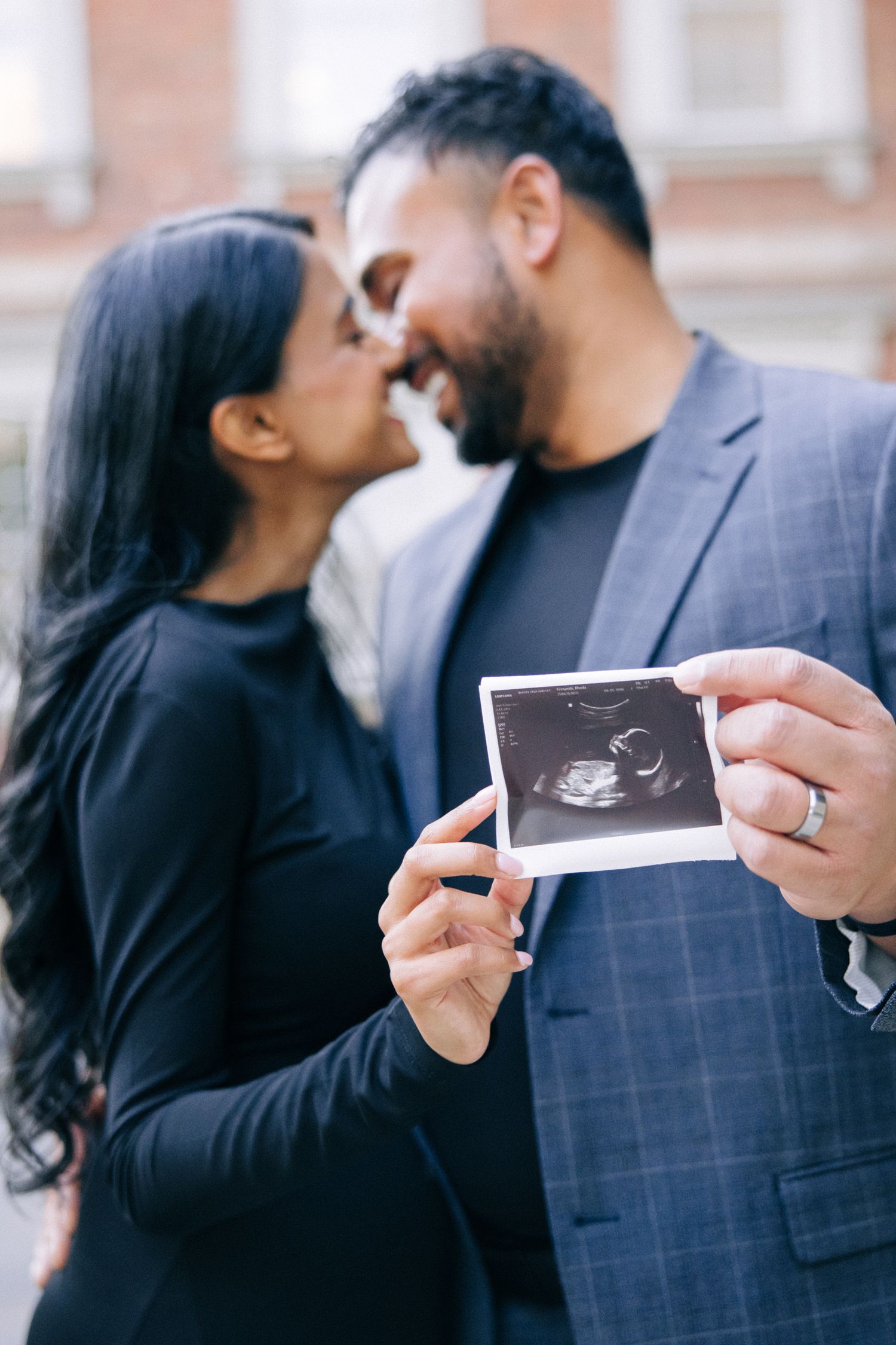 A couple shares an intimate moment while holding up a sonogram photo showing their expected baby.