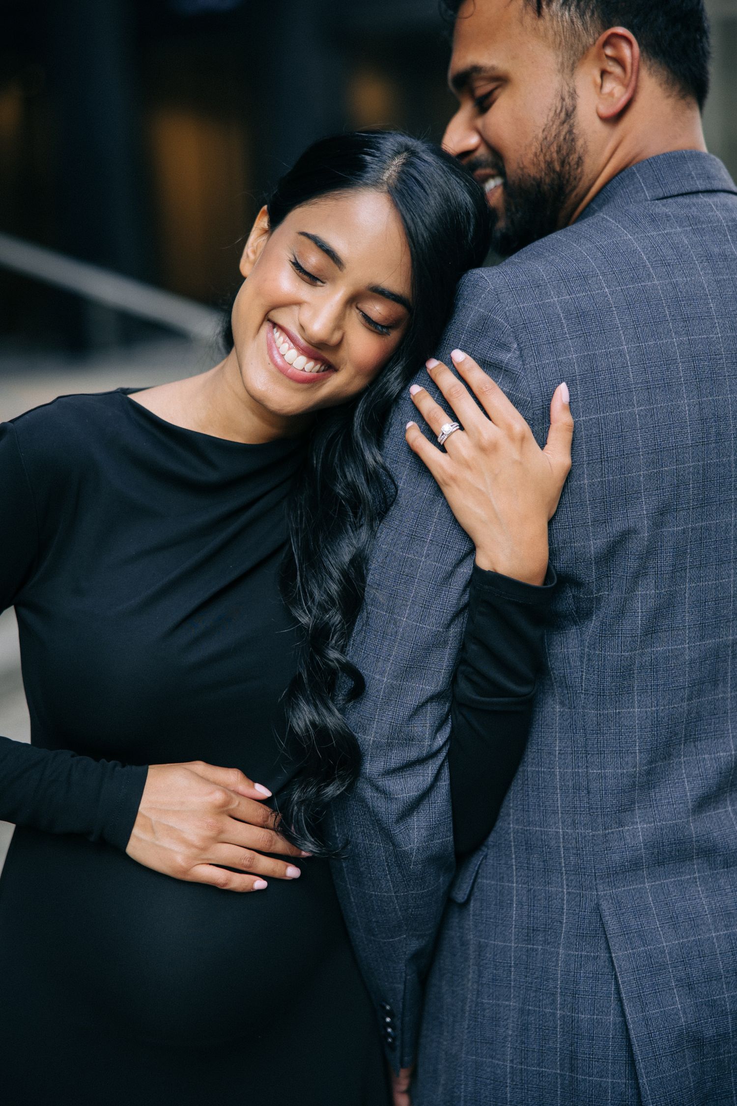 A romantic couple shares an intimate moment together, with the woman in black and man in gray suit embracing and smiling.