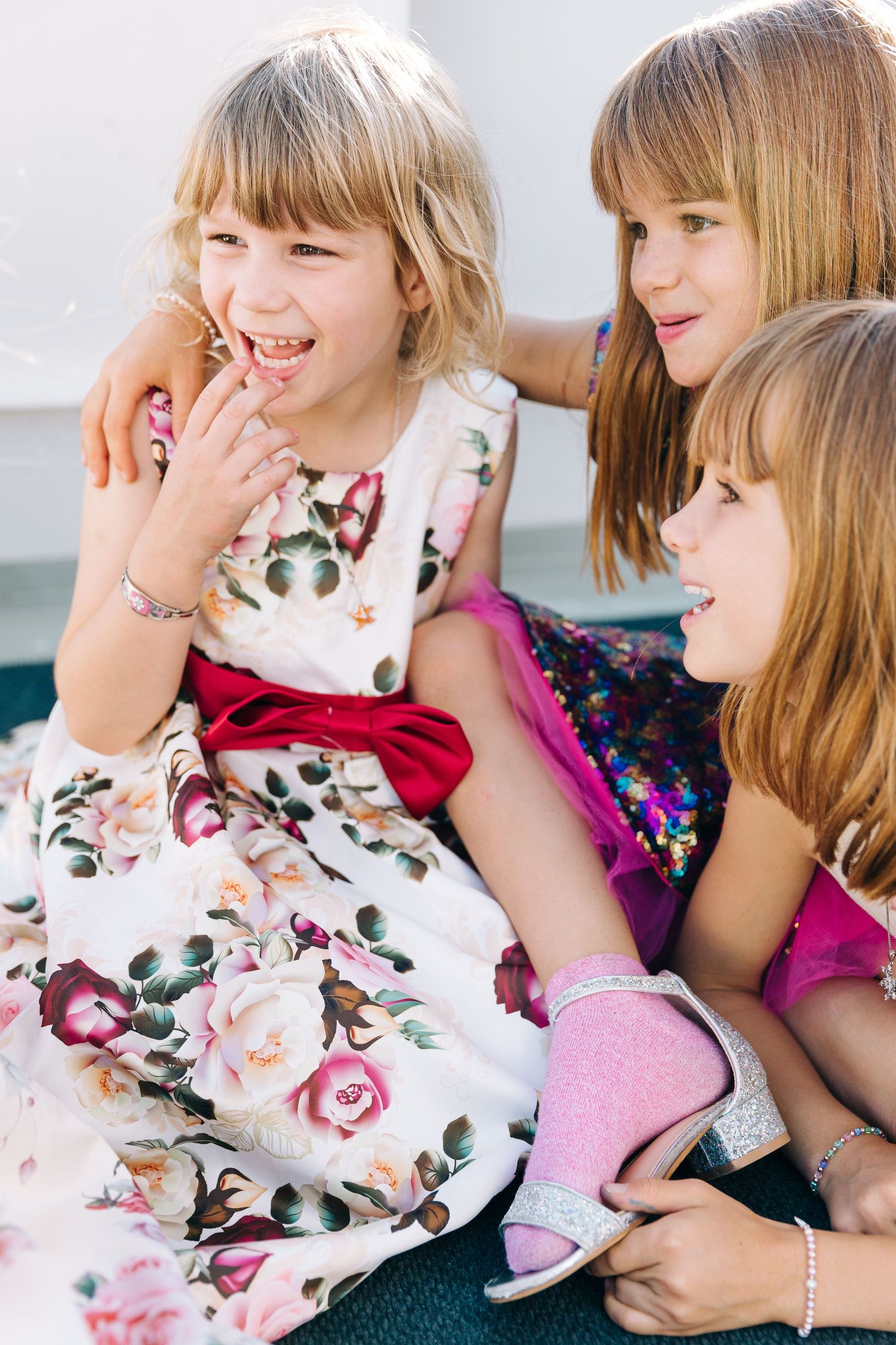 Three young children in floral dresses sharing a laugh together.