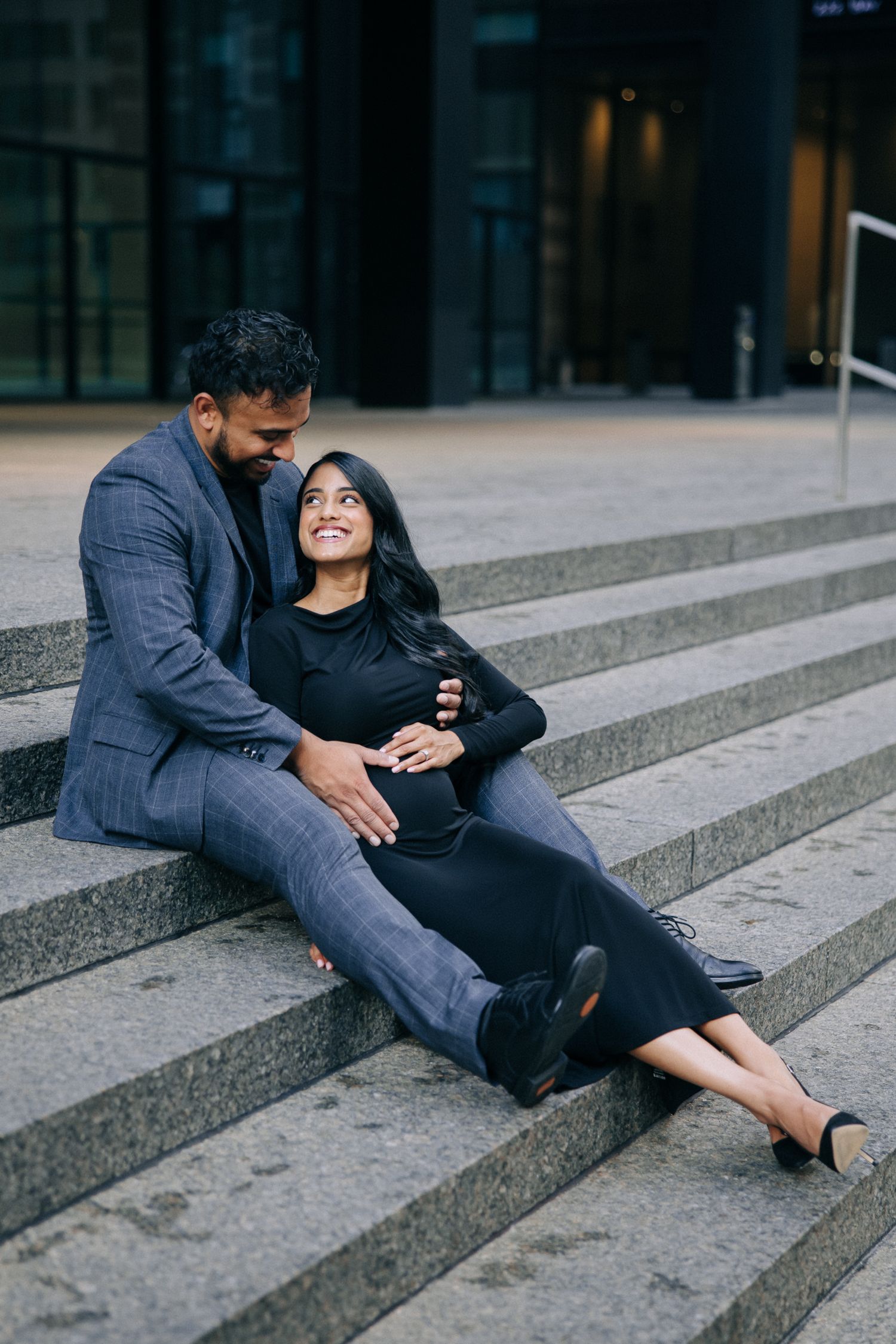 A couple share a romantic moment while relaxing on concrete steps in an urban setting during evening hours.
