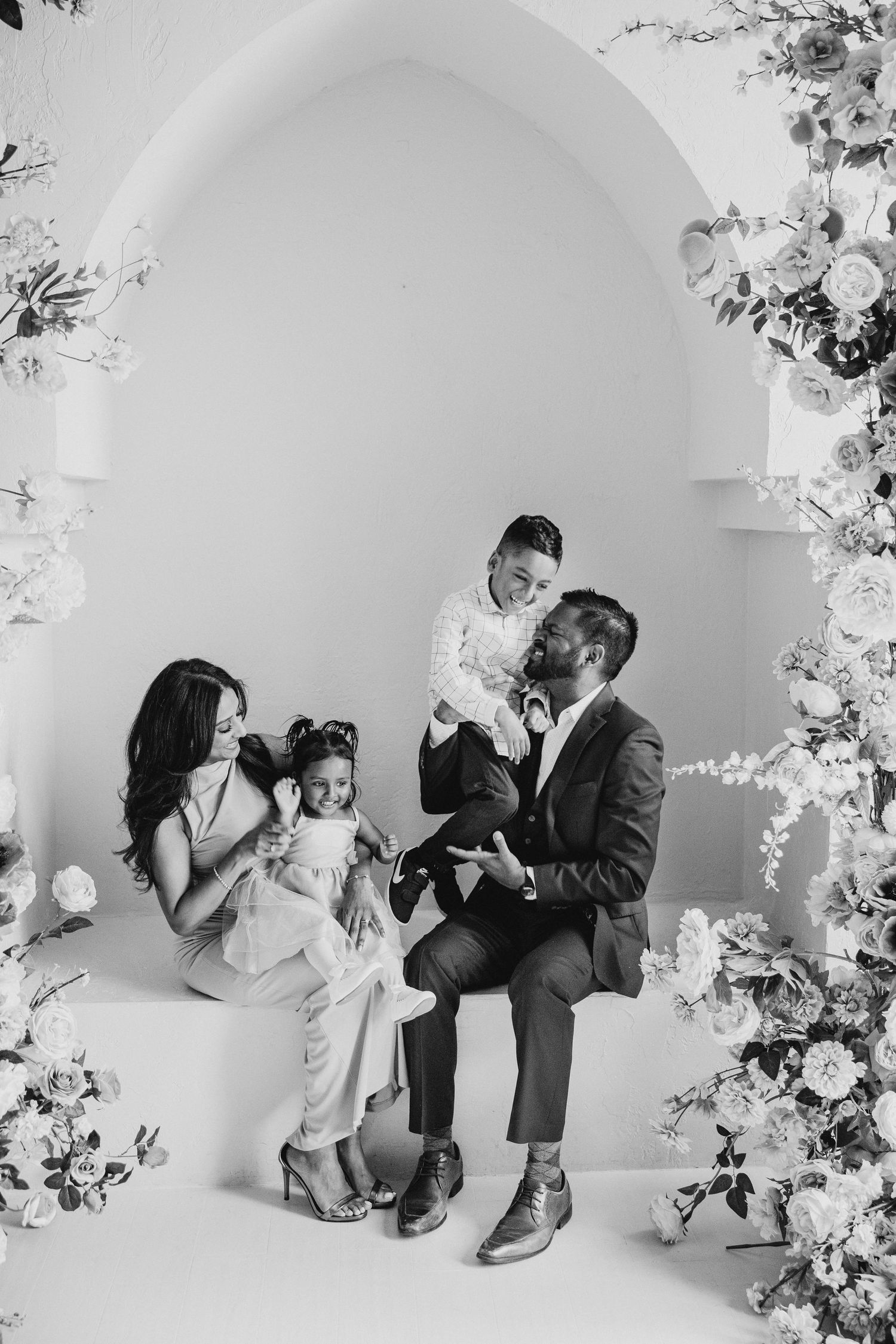 A family poses together under a white archway decorated with floral arrangements.