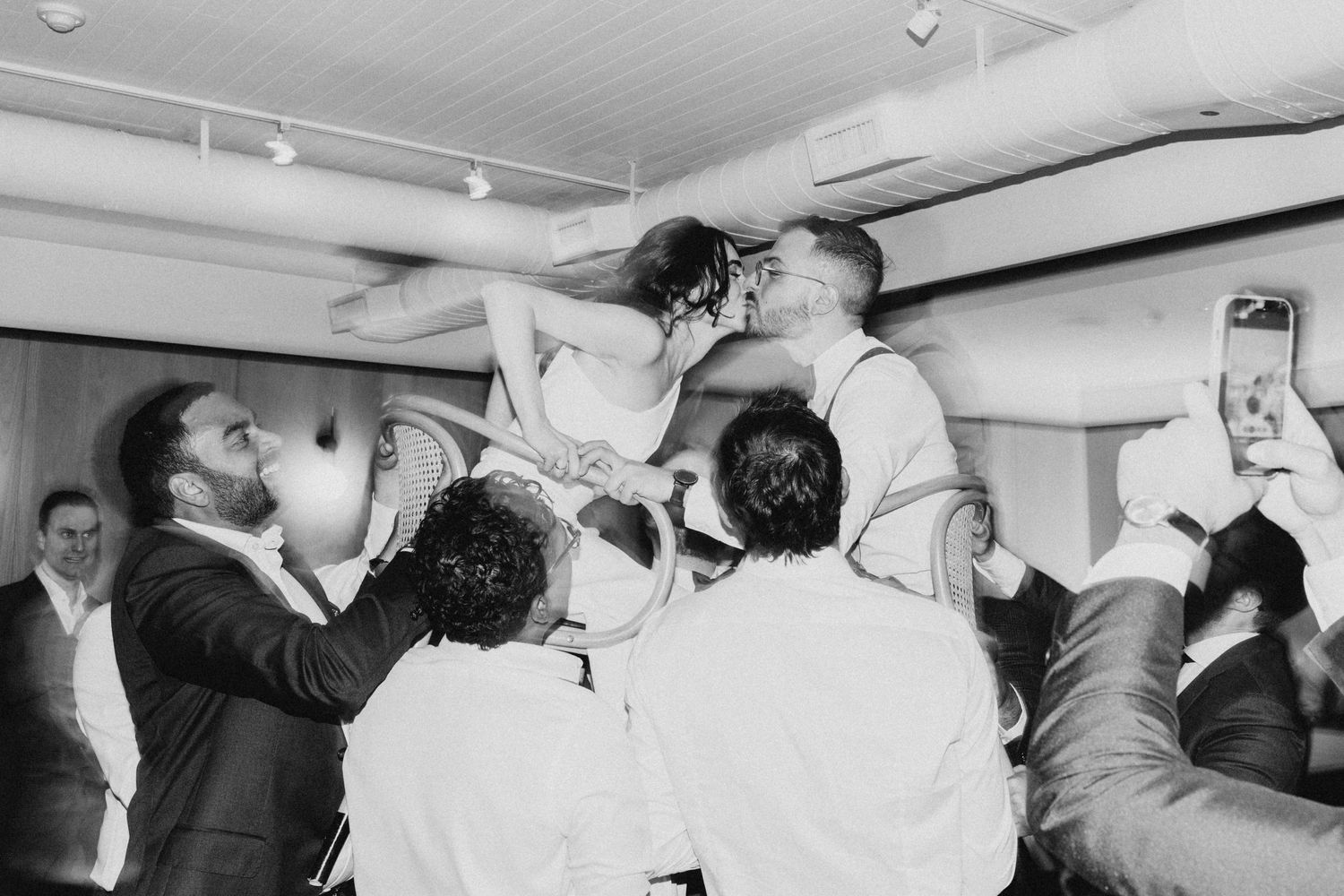A joyous celebratory moment captured in black and white as a group is lifted up by others at an indoor celebration.