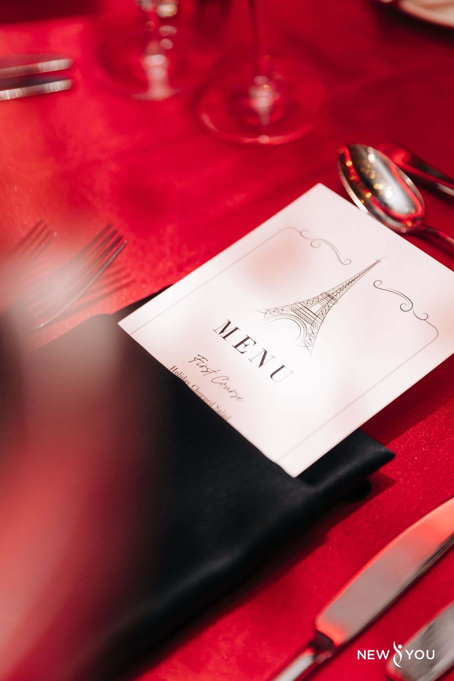 A menu card with Eiffel Tower design on red tablecloth at formal dining setting.