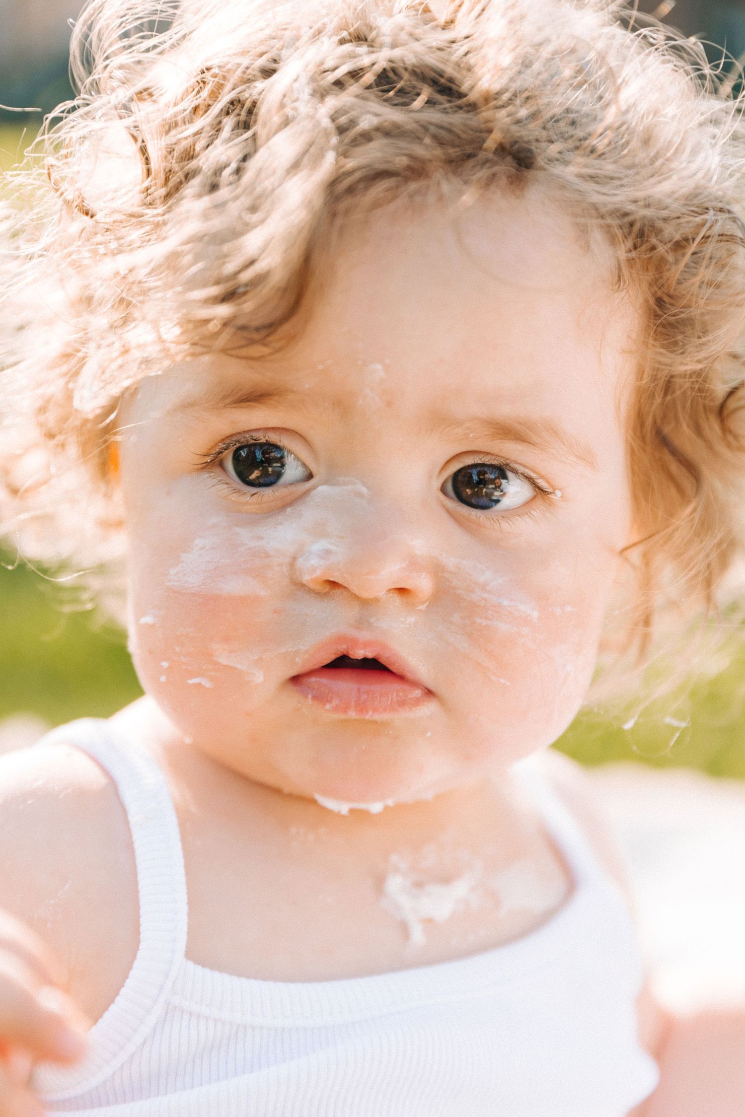Close-up portrait of a toddler with curly hair and messy sunscreen on their face.