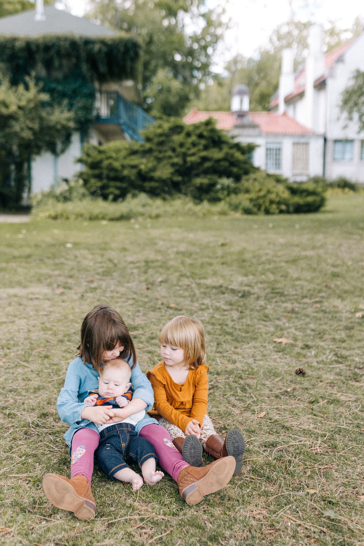 Children sitting together on grass with a baby in front of a house.