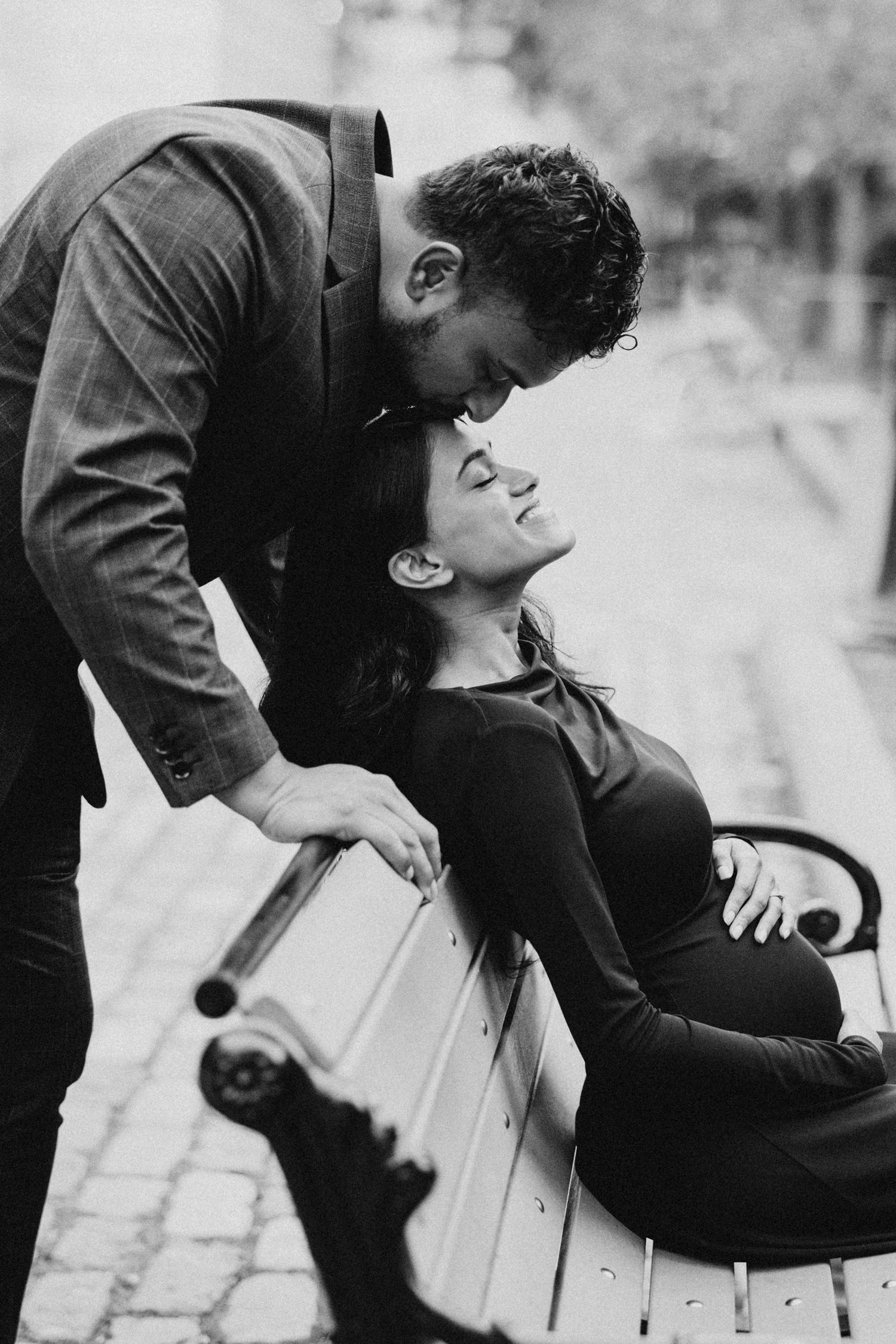 A romantic black and white photograph of a couple sharing an intimate moment on a park bench outdoors.