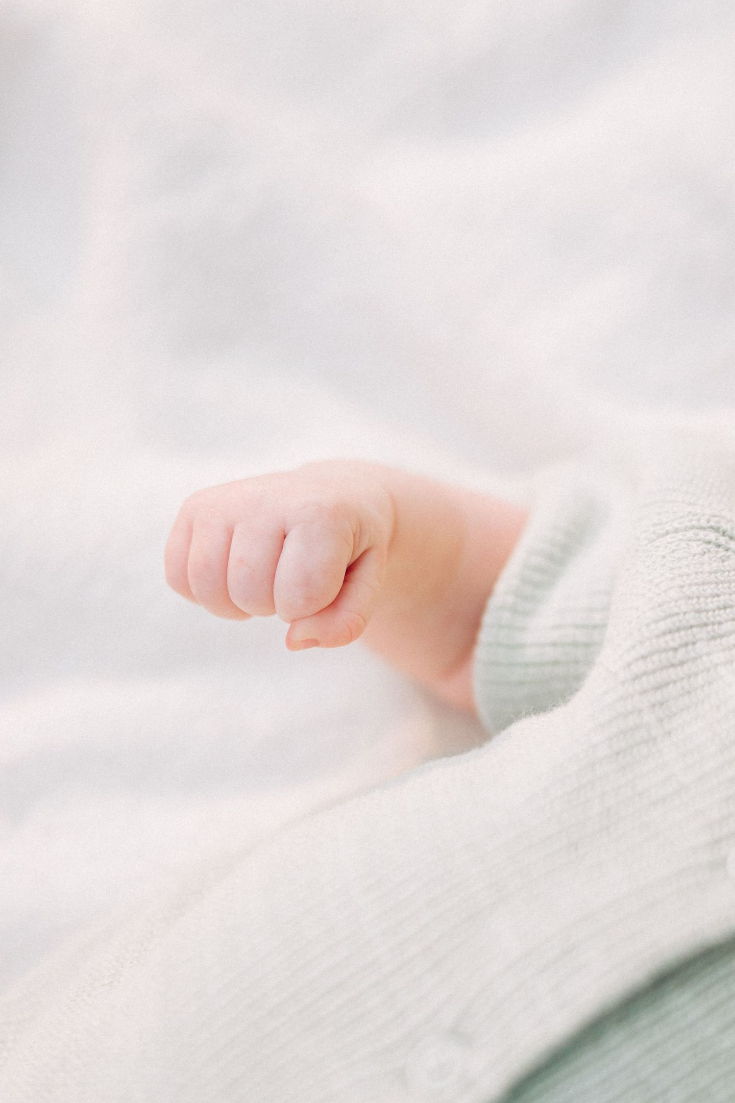 Close-up of a tiny baby's hand against a soft white background.