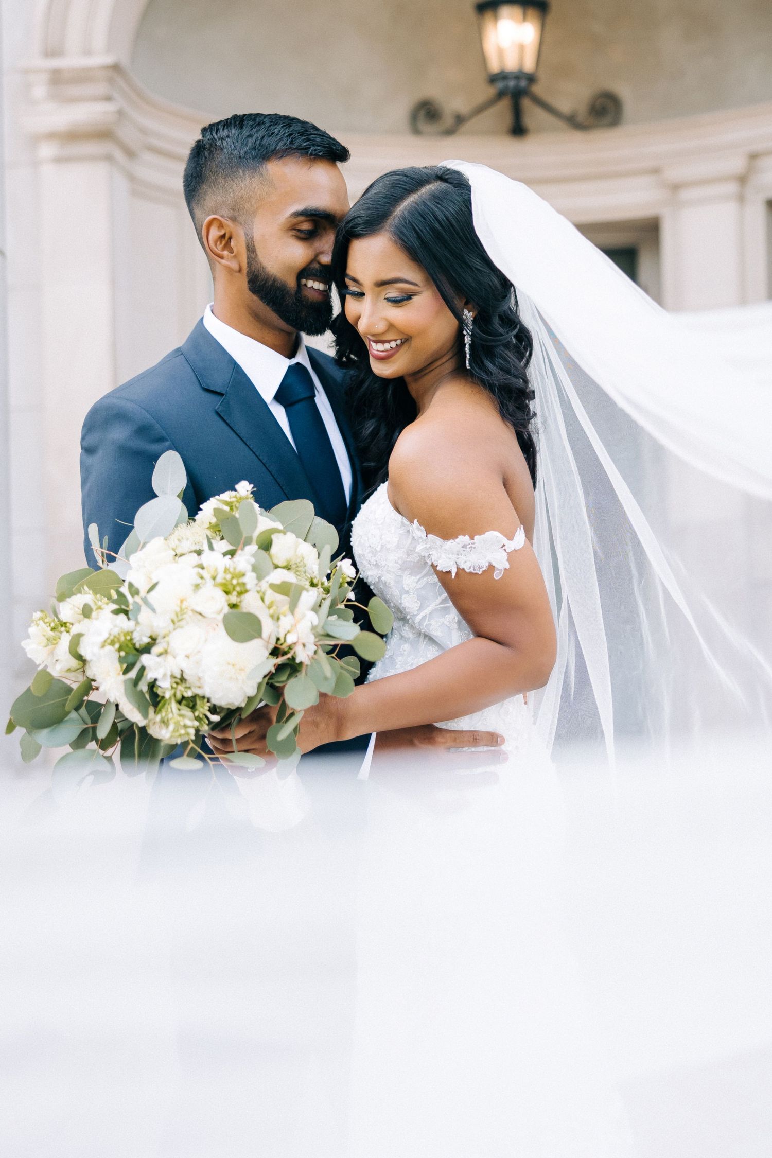 A beautiful wedding couple shares an intimate moment while the bride holds a stunning white floral bouquet.