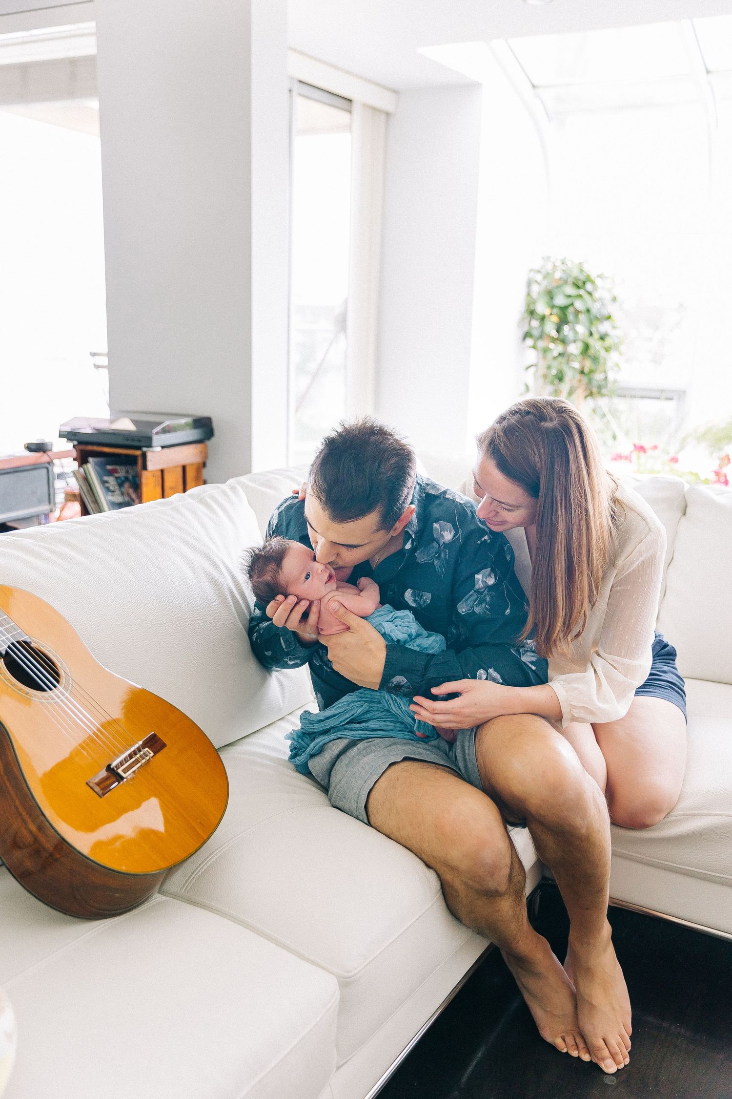Family sharing a tender moment together on a white couch with an acoustic guitar nearby.