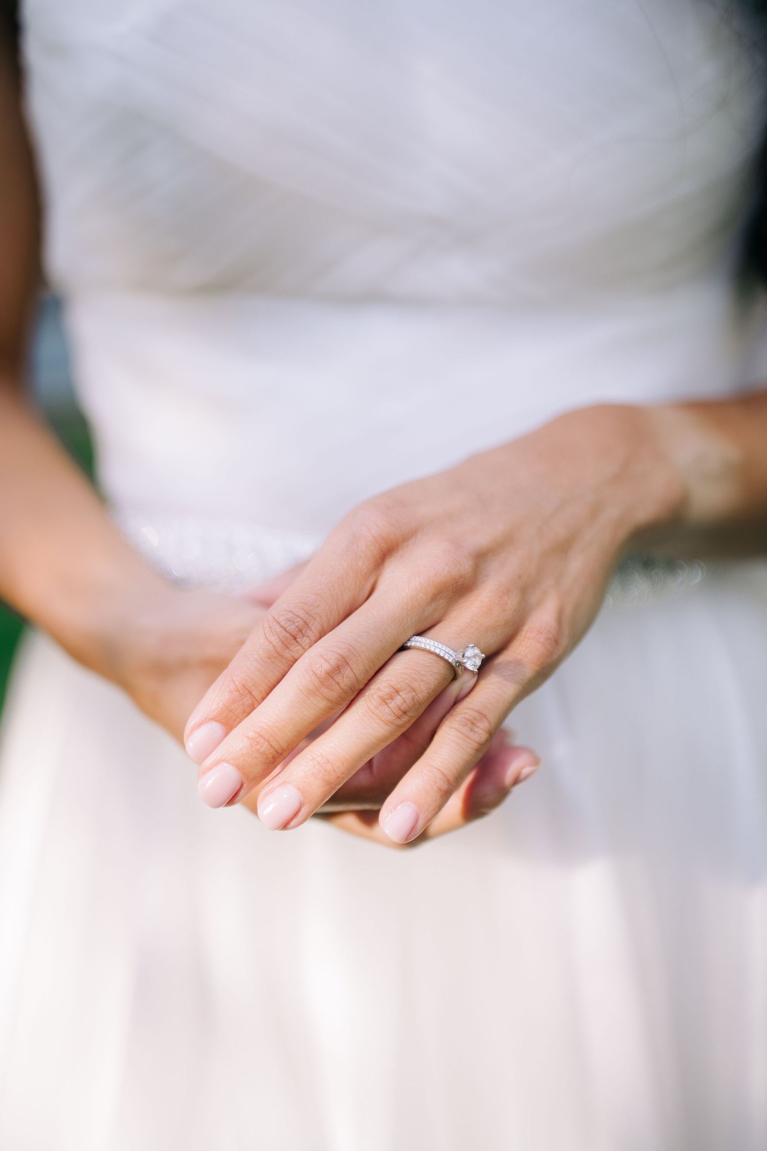 Close-up shot of an elegant engagement ring on a hand against a white dress.