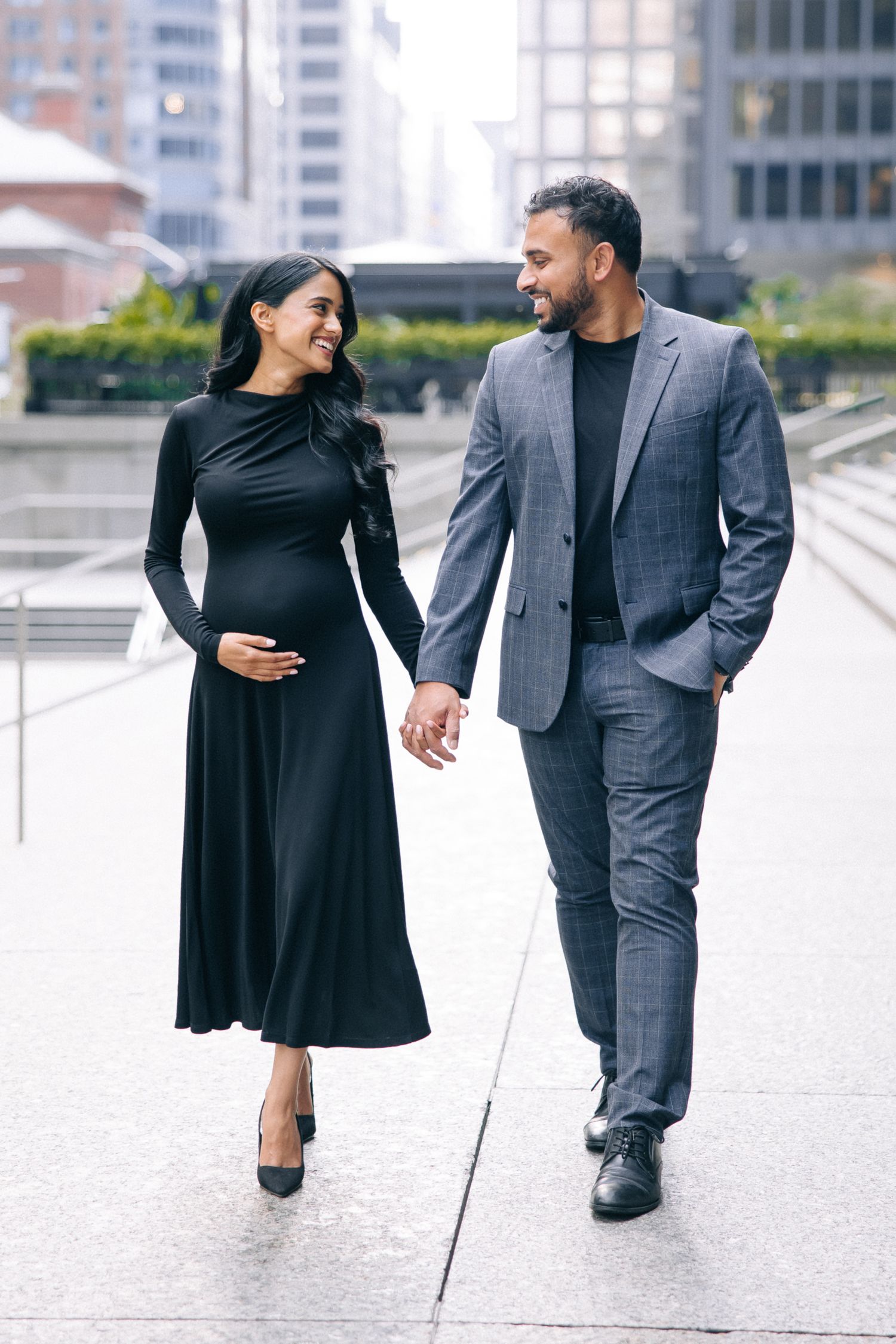 A stylishly dressed couple holding hands while walking in an urban setting, with a pregnant woman in a black dress.