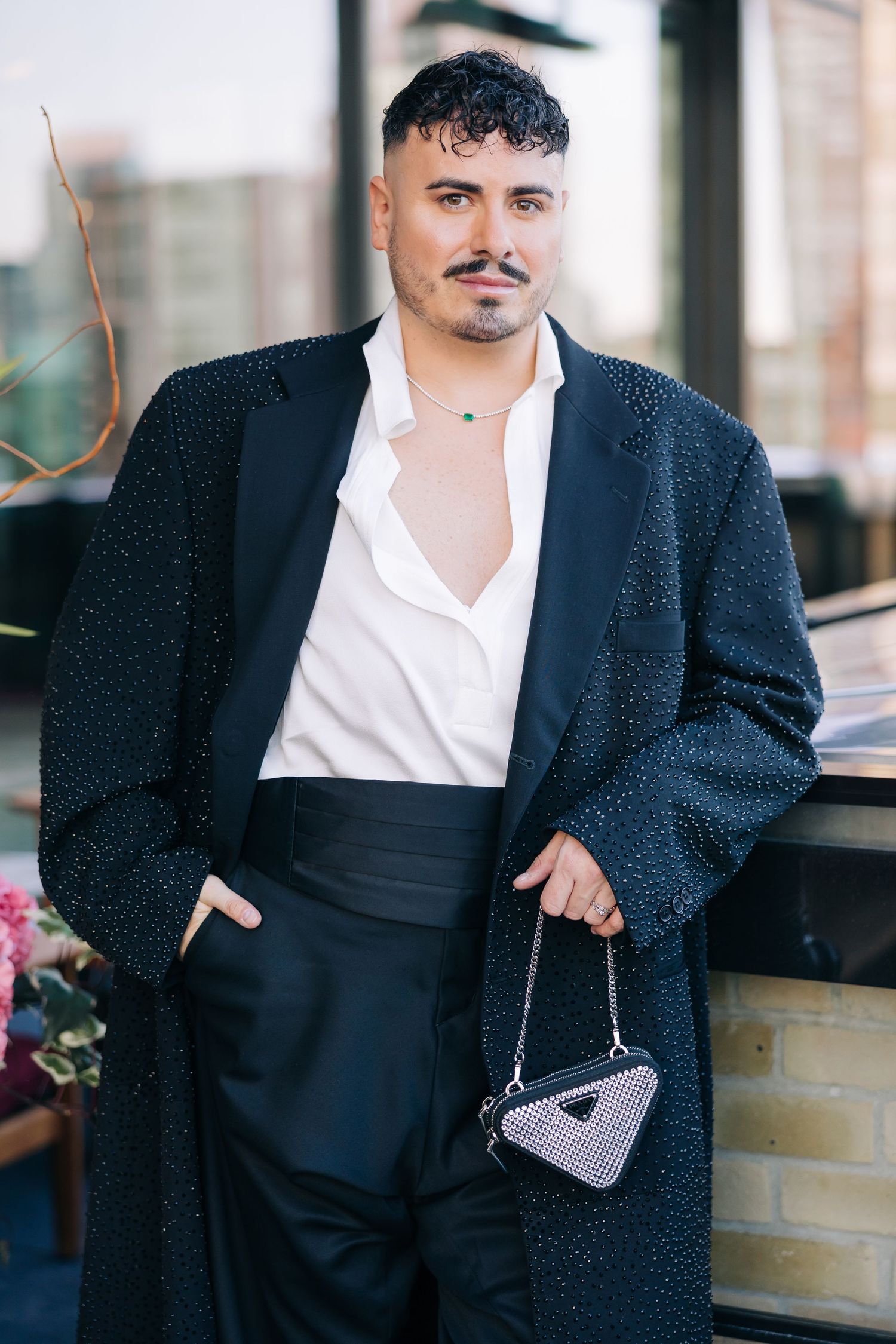 A stylish outfit featuring a long black coat, white button-down shirt, and a small triangular handbag accessory.