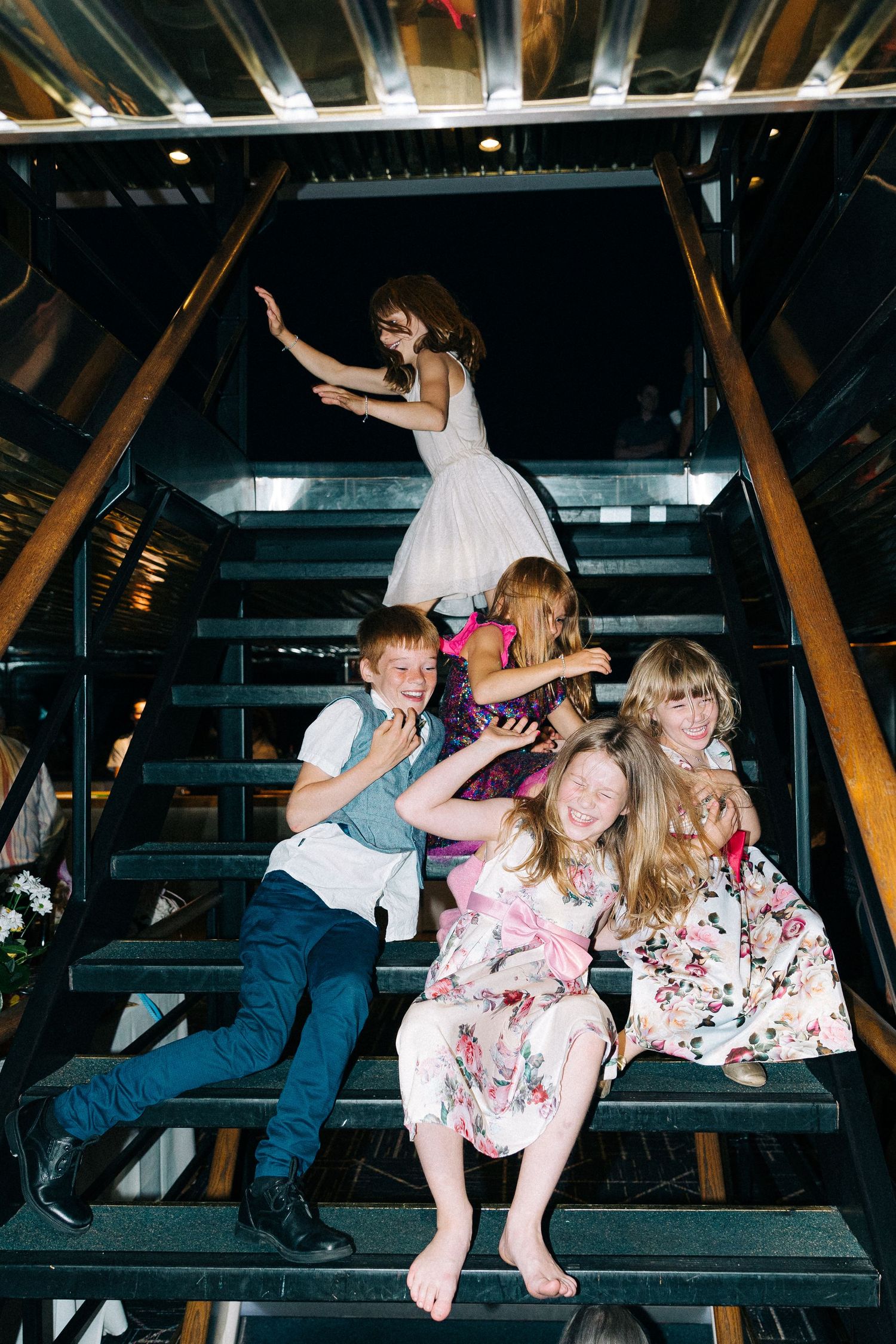 A fun group photo on wooden stairs with people in floral dresses striking playful poses.