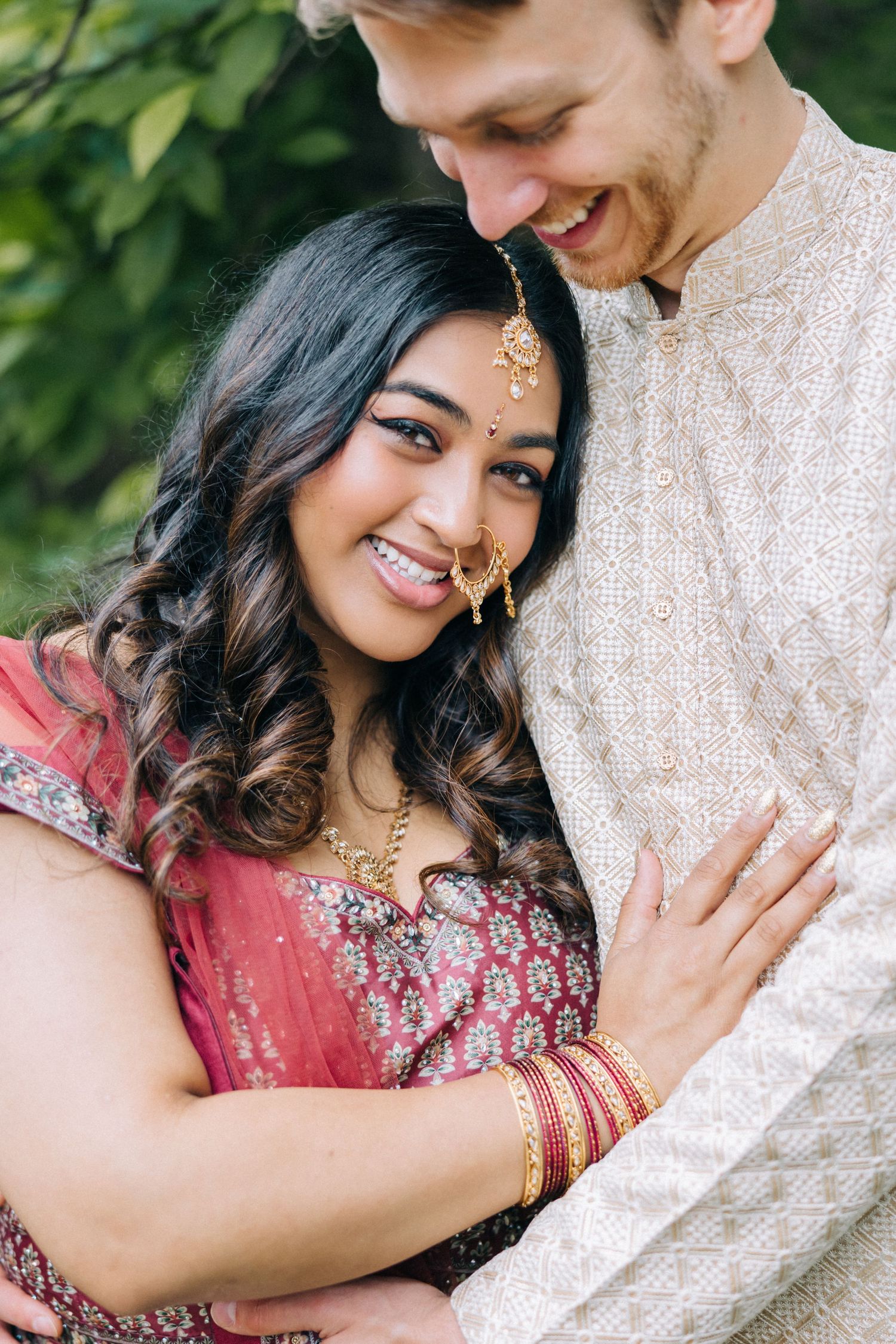 Intimate portrait of couple in traditional Indian wedding attire embracing outdoors.