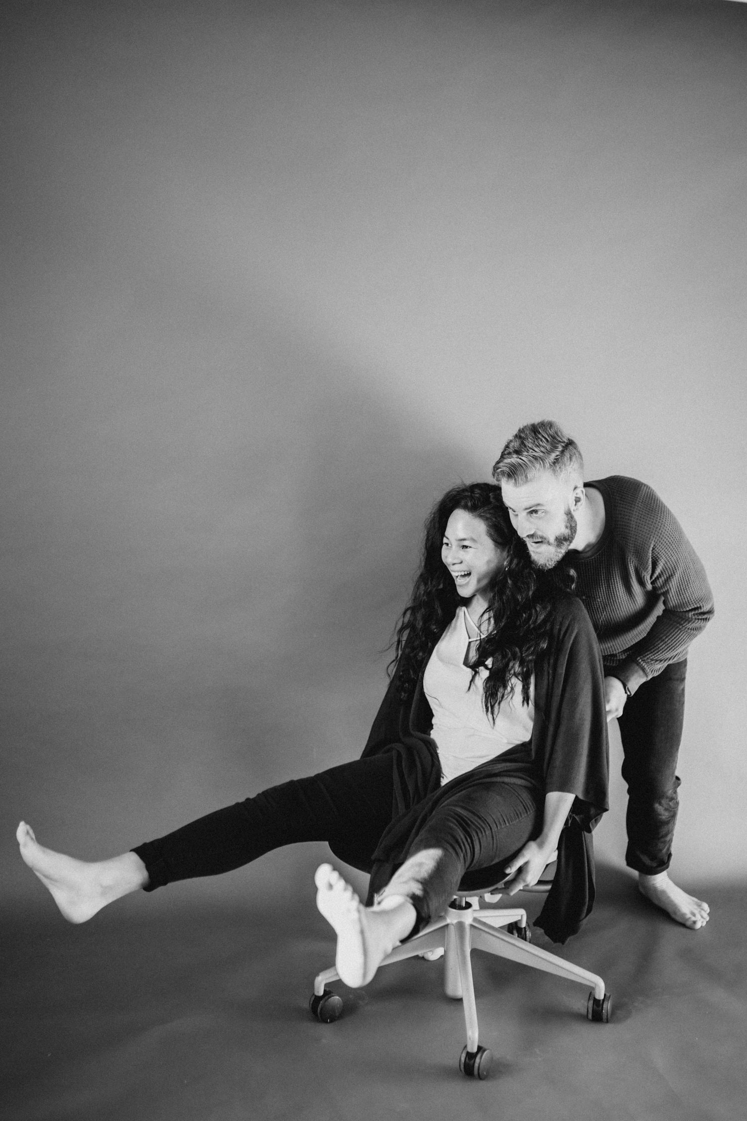 Playful black and white photo of couple having fun with office chair.