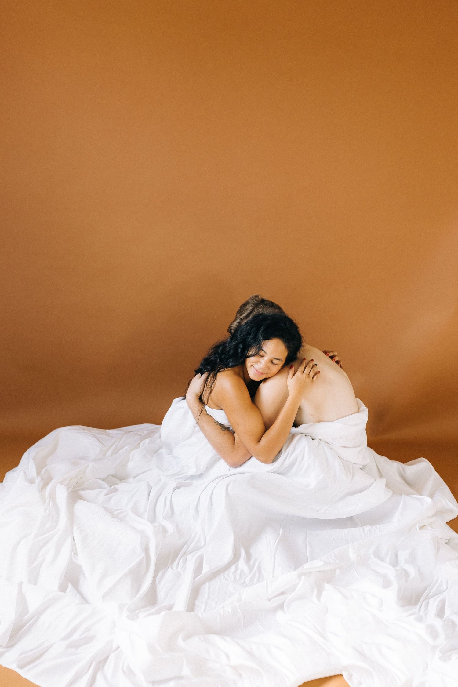Person wrapped in flowing white bedding poses against warm brown background in a peaceful sleeping position.