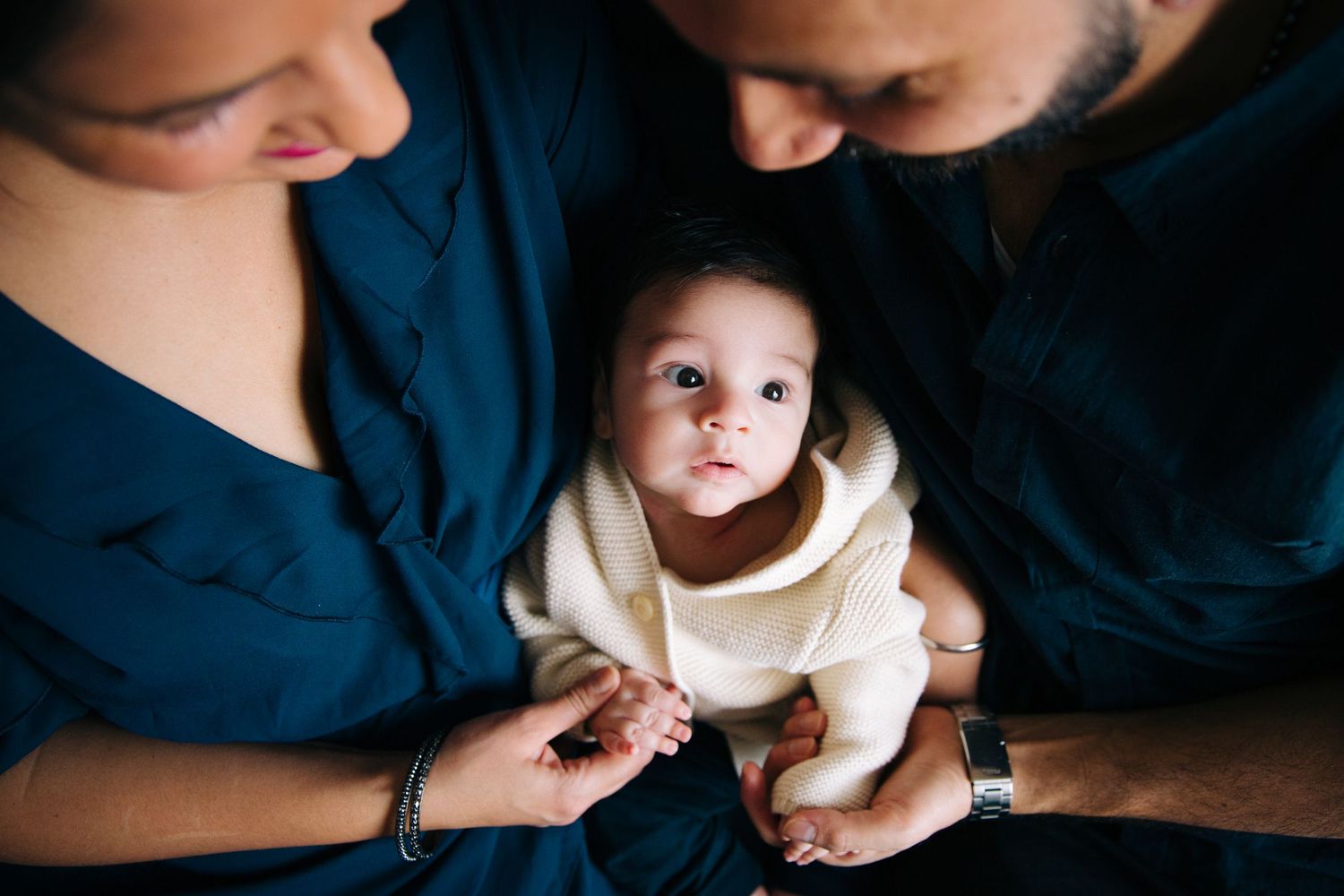 Close up view of parents gazing lovingly at their baby wearing a cream colored outfit.