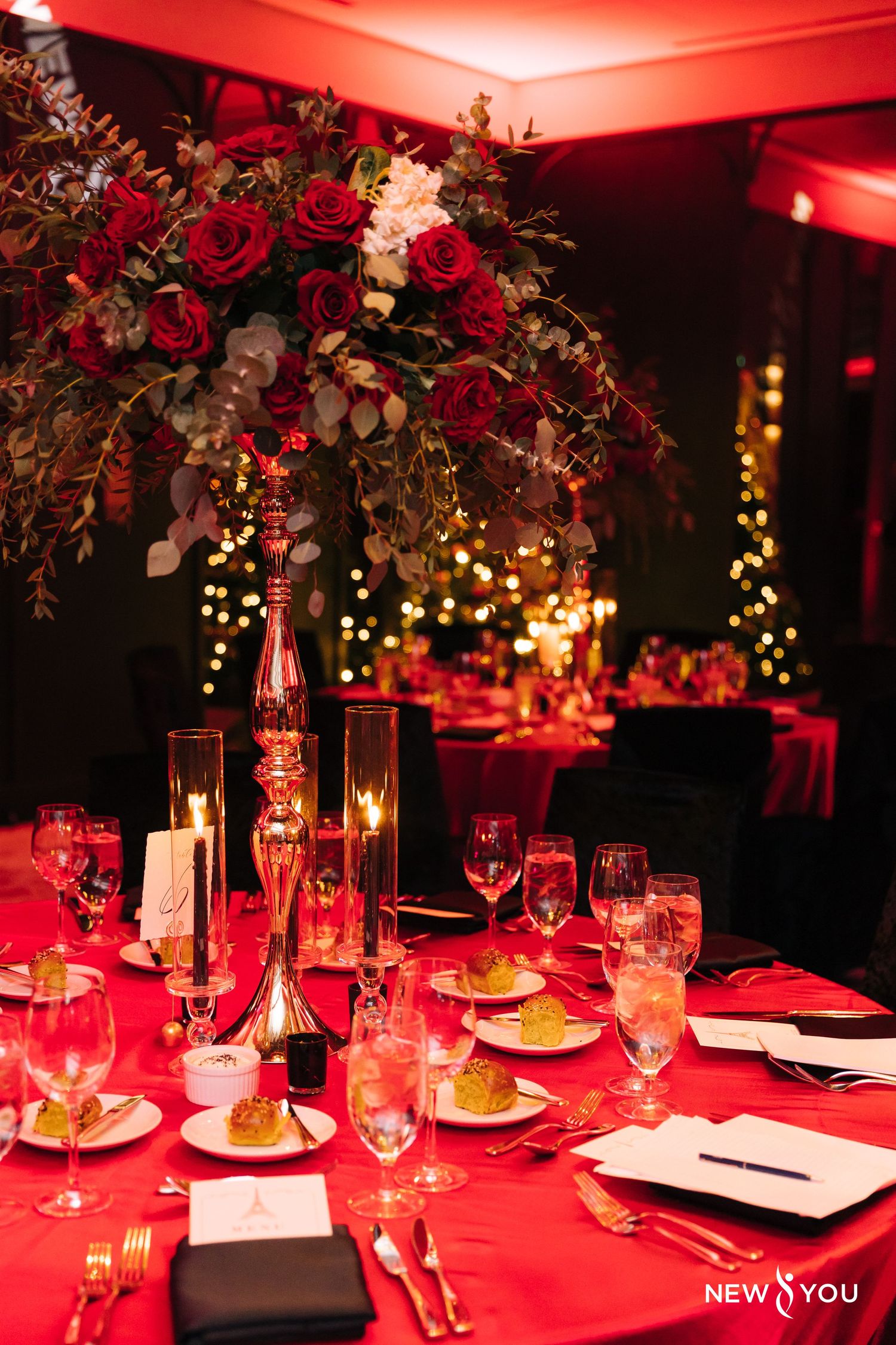 Elegant wedding reception table with red tablecloth, floral centerpiece and romantic candlelight under dramatic red lighting.