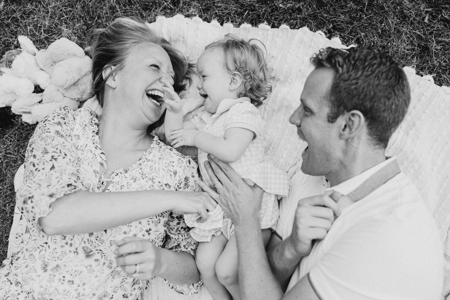 A joyful family lying on grass sharing a candid laughing moment together.