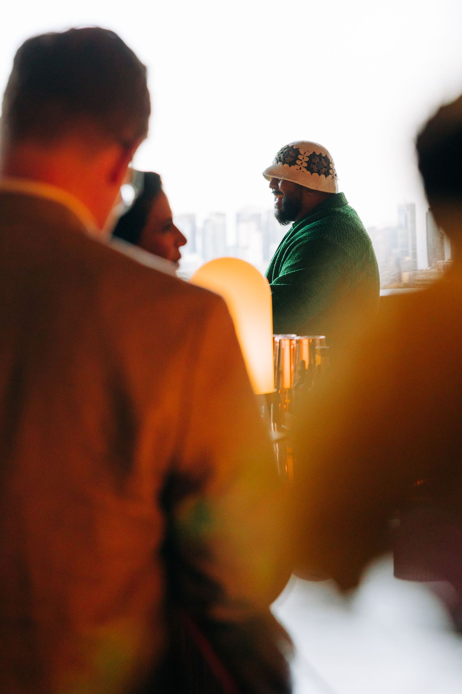 A person in a green shirt and hat seen through a soft-focus crowd during a gathering or event.