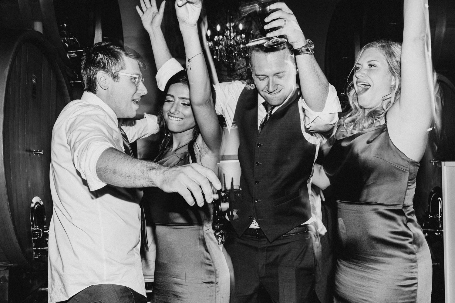 Black and white photo showing a group of people dancing and celebrating together at a party with arms raised in joy.