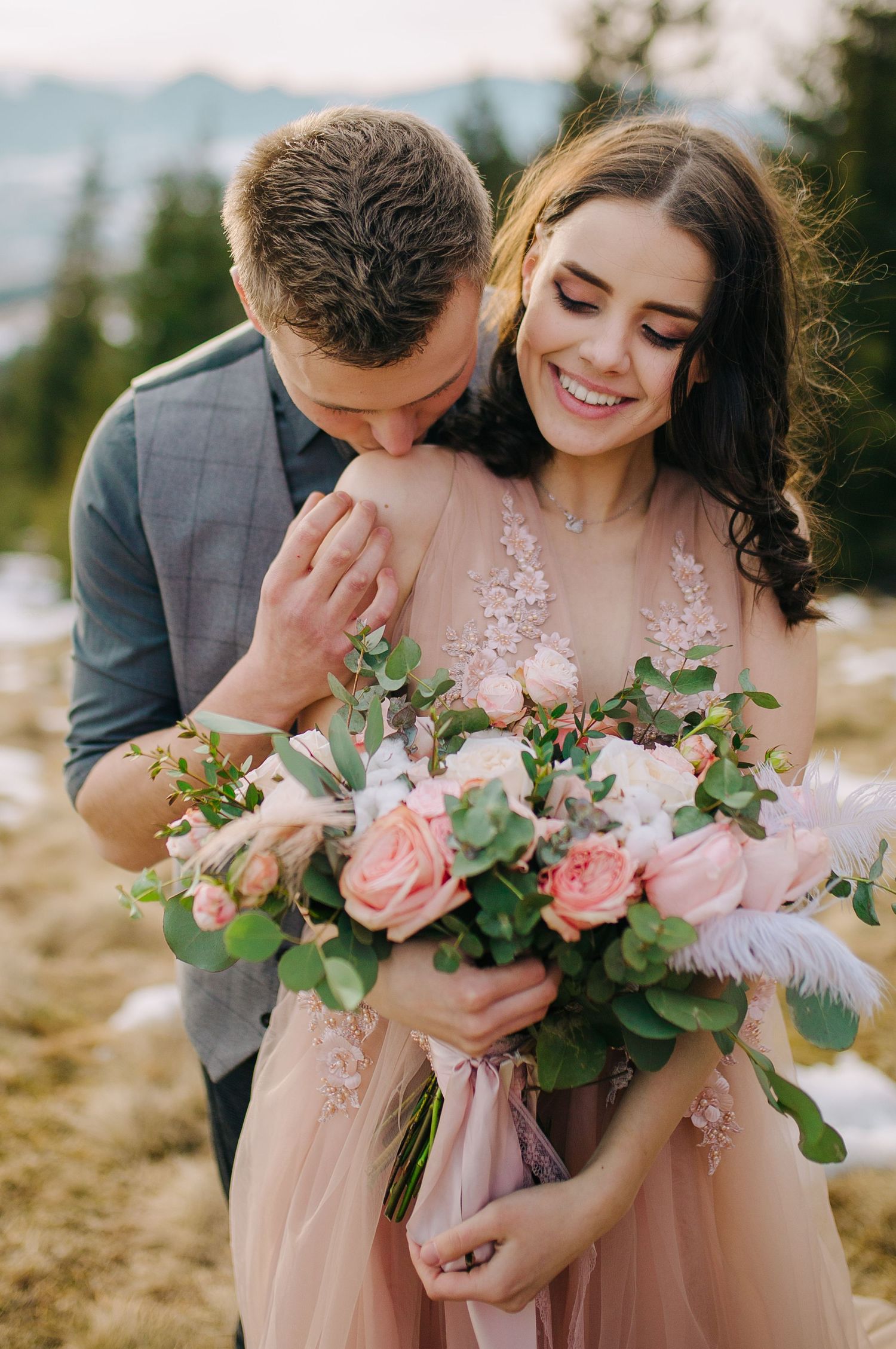 A romantic outdoor portrait of a couple embracing, with the bride holding a beautiful pink and green floral bouquet.
