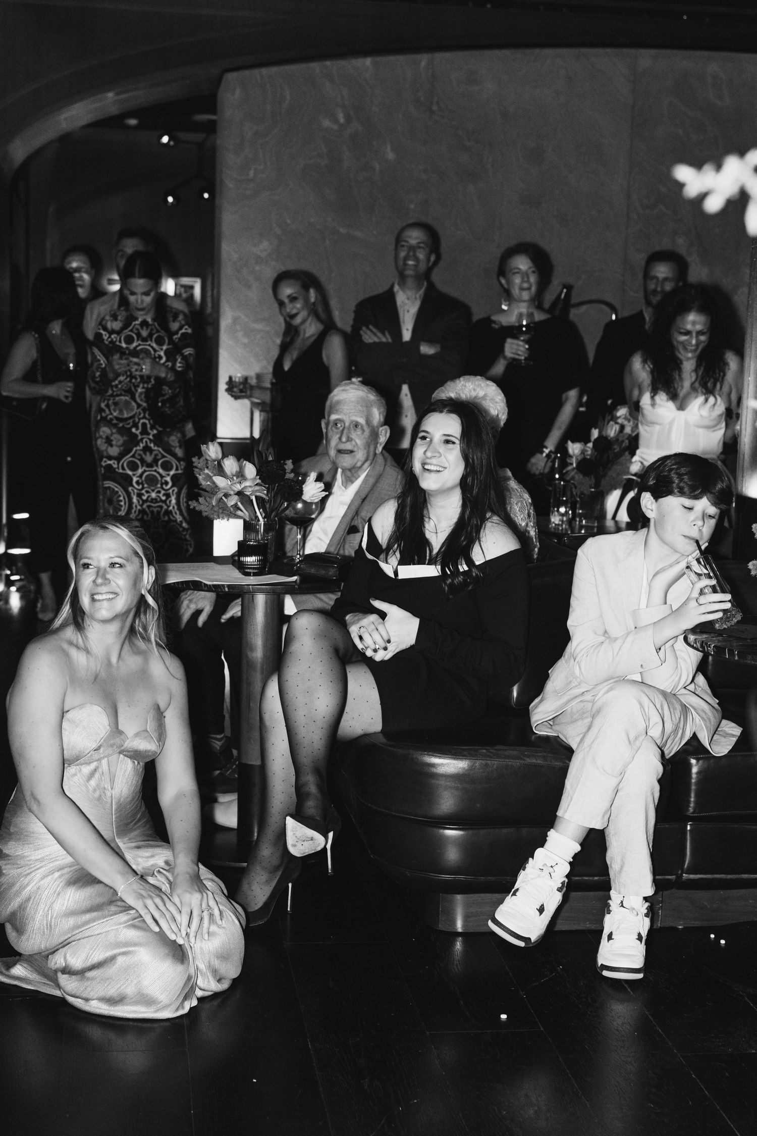 Black and white photo of party guests seated in theater-style seating at a nightclub or event space.