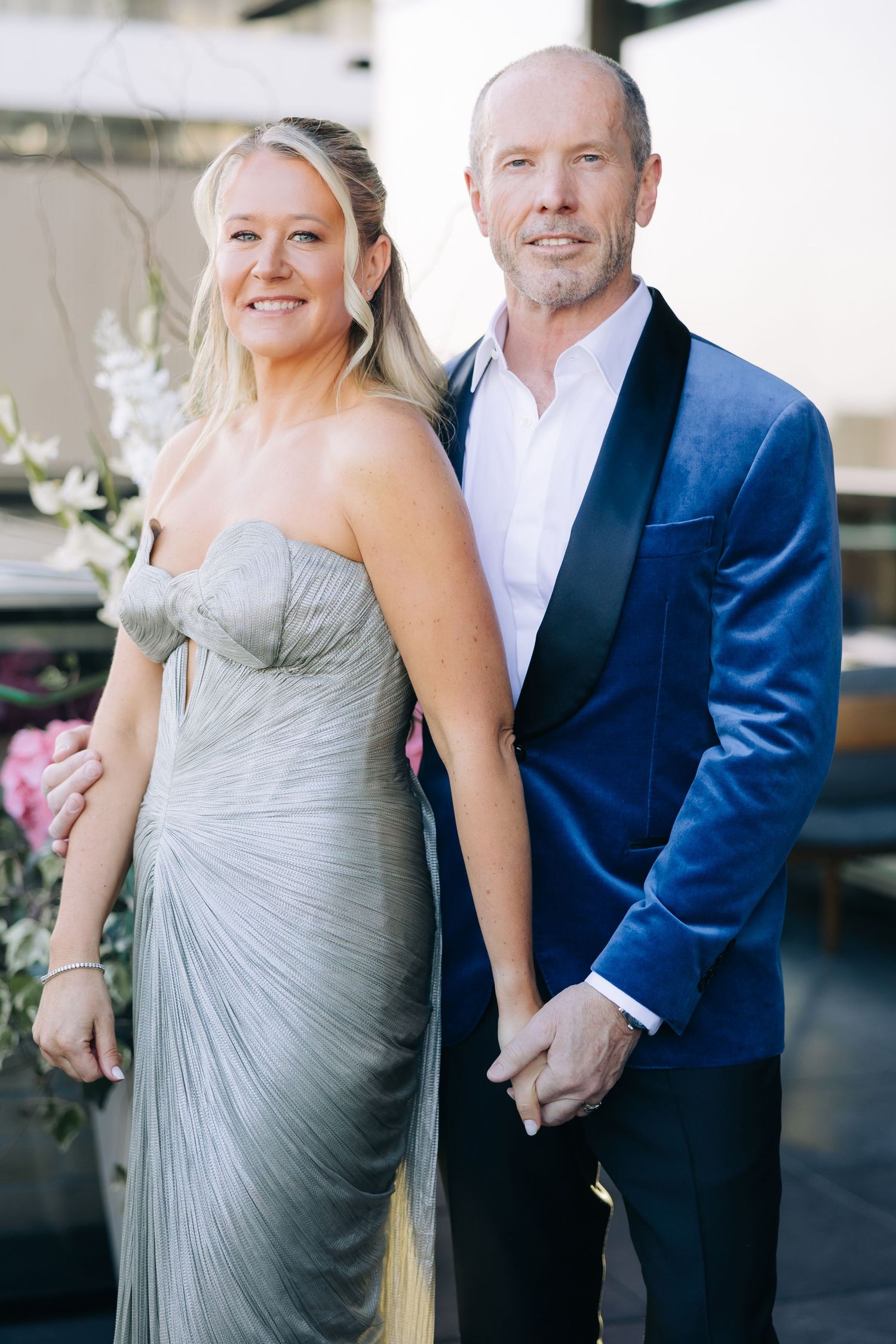 Elegant couple in formal attire posing together at an outdoor venue.