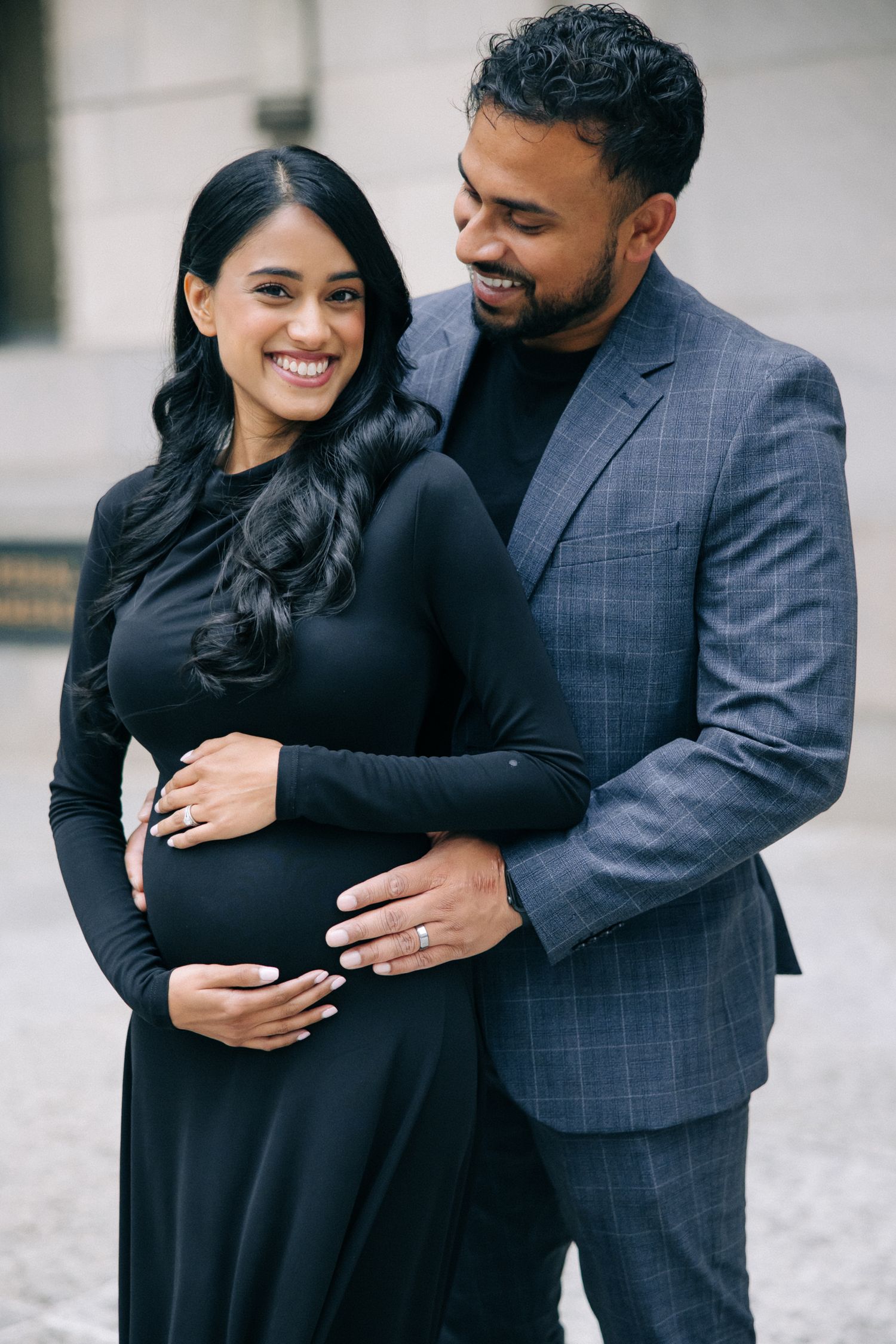 Couple in complementary formal wear smiling and embracing outside classic architecture.