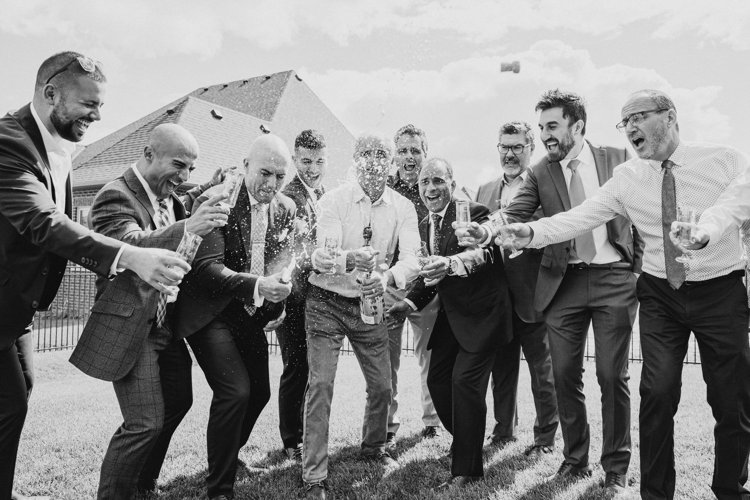 A black and white photo of a cheerful group toasting and celebrating outdoors with champagne bottles.
