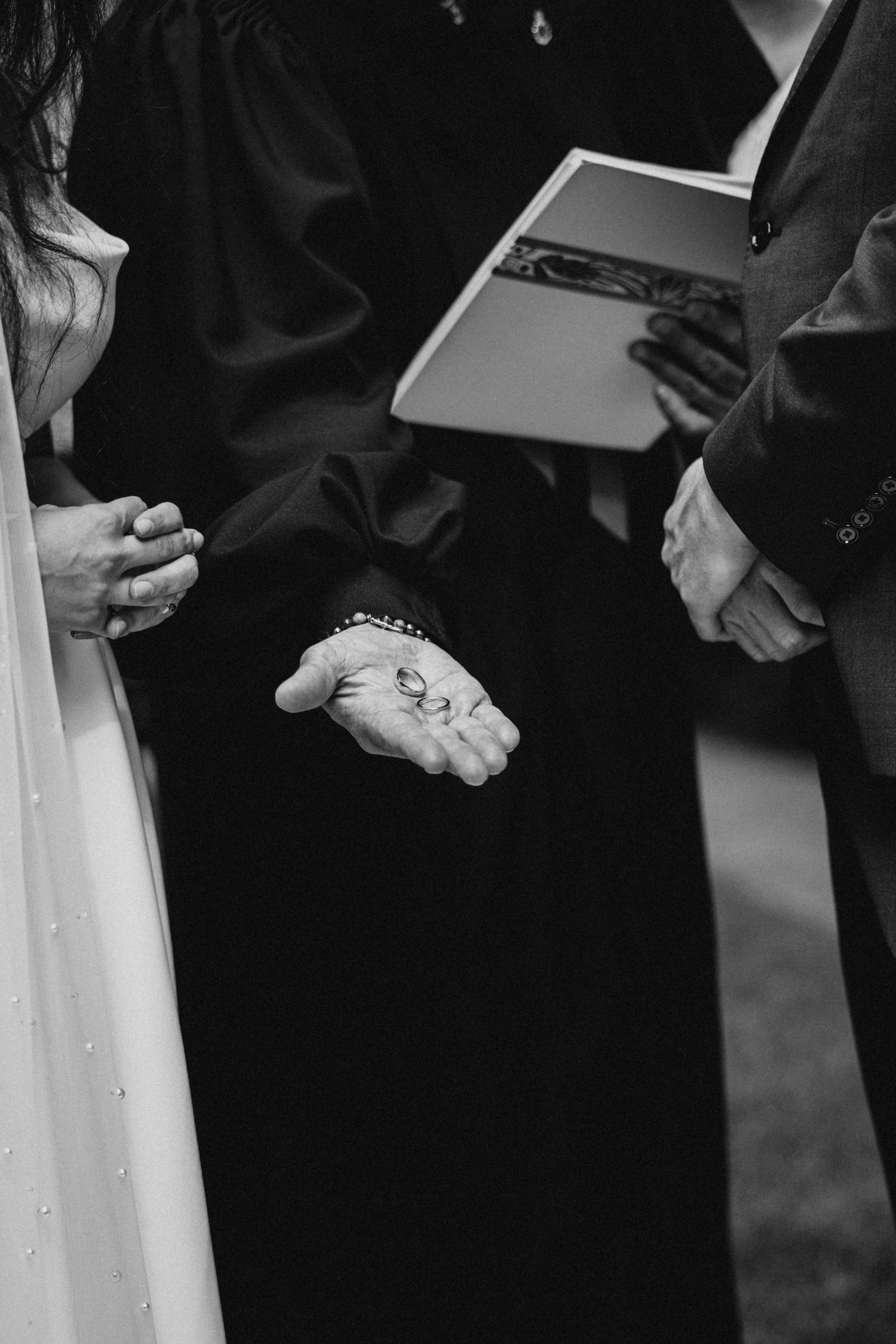 A black and white photograph showing wedding ceremony hands and a held book during a marriage service.