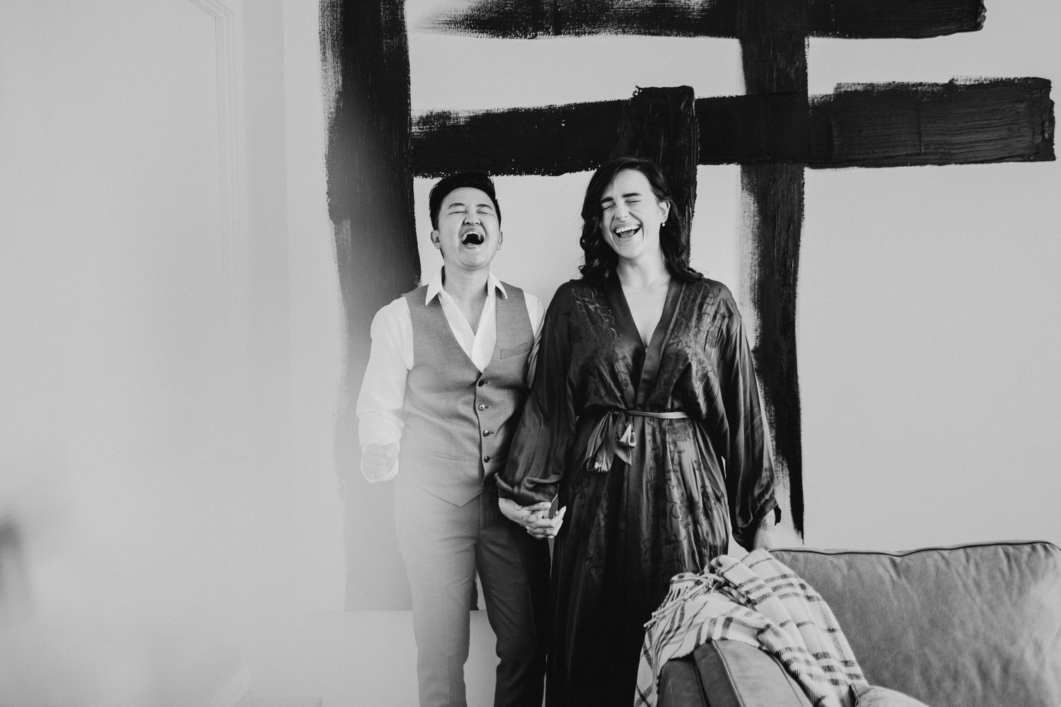 A black and white candid photo of a couple laughing together during an intimate indoor photoshoot.
