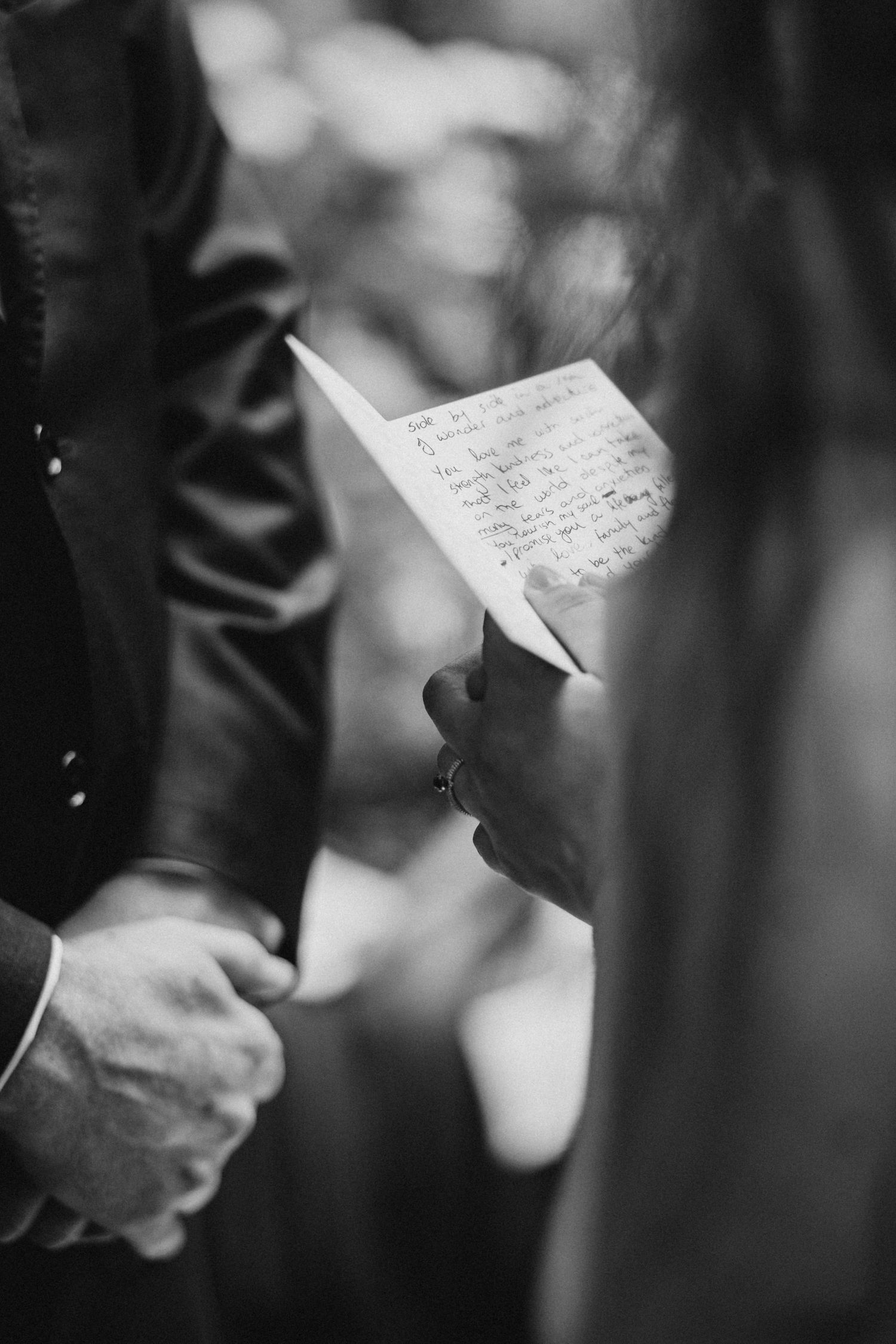 A person in formal attire holds handwritten wedding vows during an intimate ceremony captured in black and white.