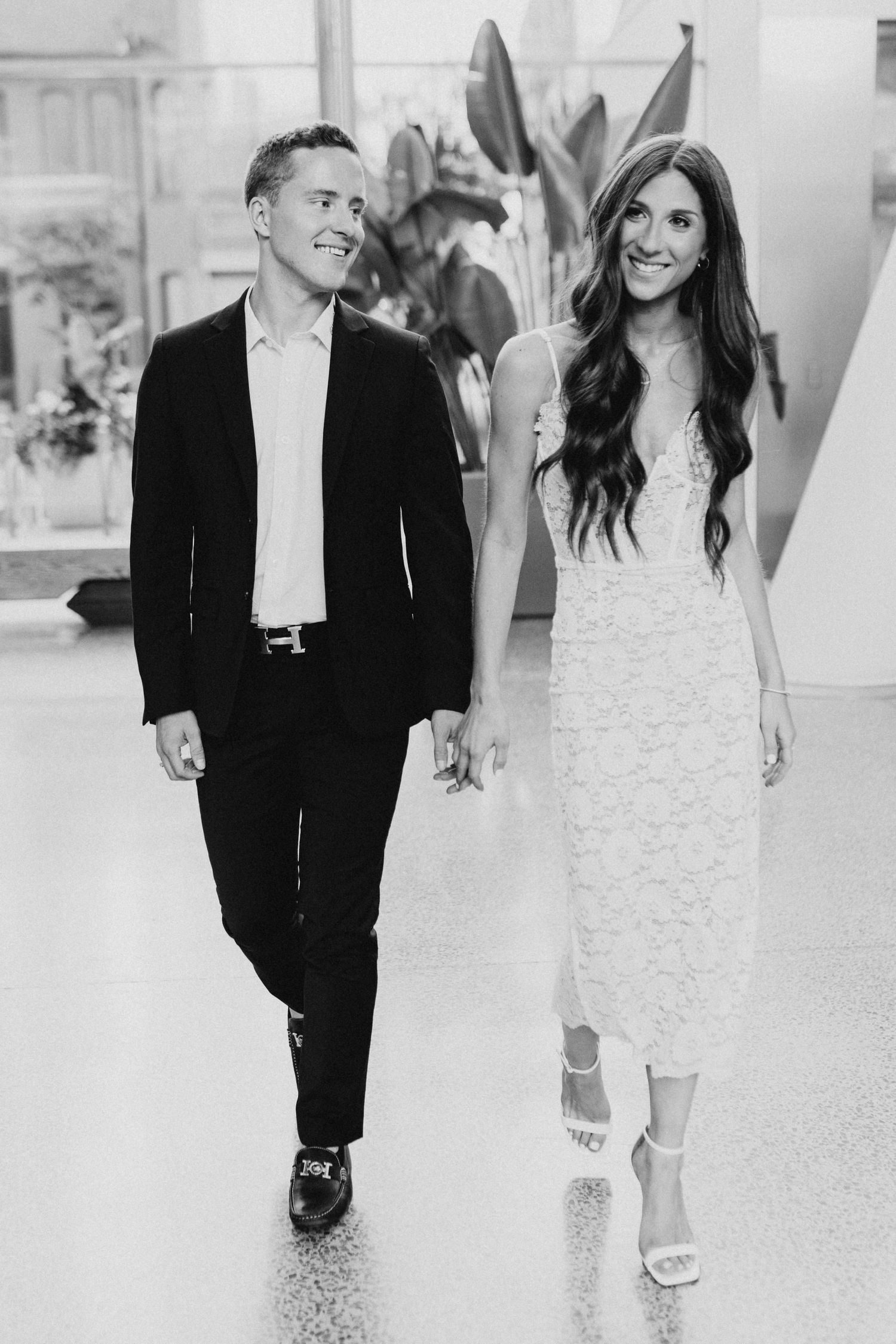 Black and white photo of stylish couple walking through modern interior space.