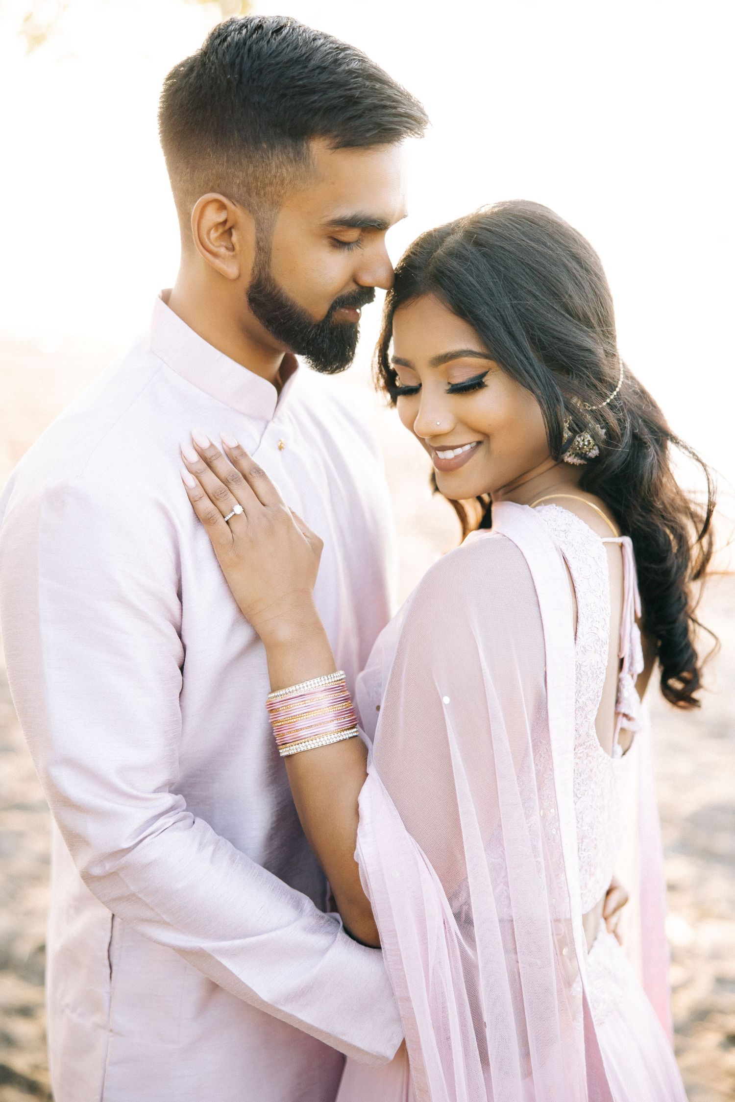 A romantic couple in matching pink and white outfits embraces during an engagement photoshoot.