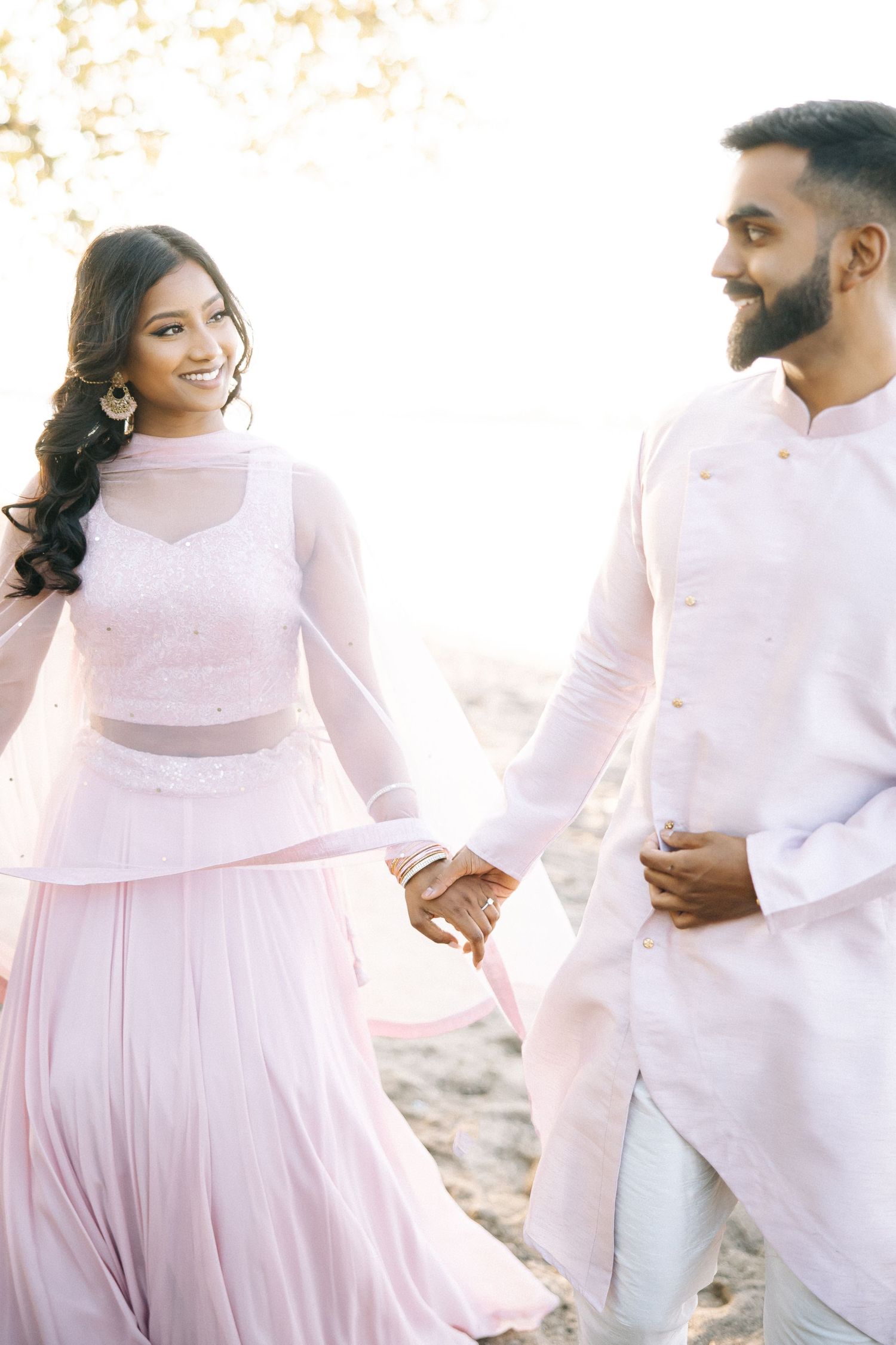 A couple in matching pink and white outfits shares a joyful moment on the beach.