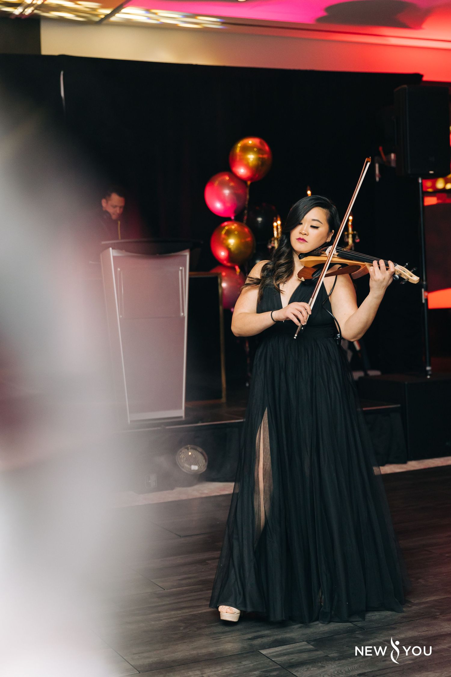 Violinist in a black evening gown performs on stage with colorful balloons in the background.