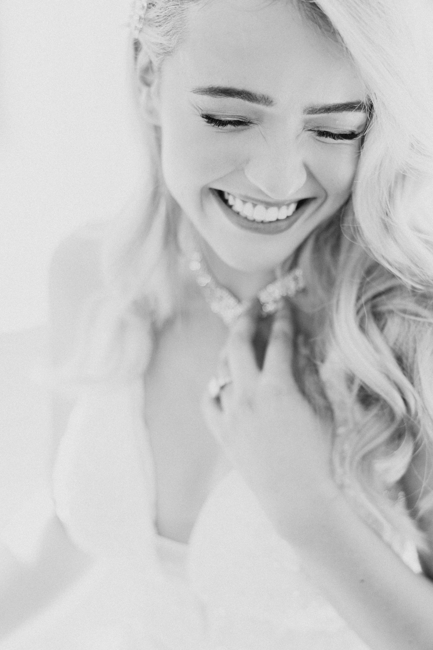 Black and white close-up portrait of a joyful bride with blonde wavy hair and a bright genuine smile.