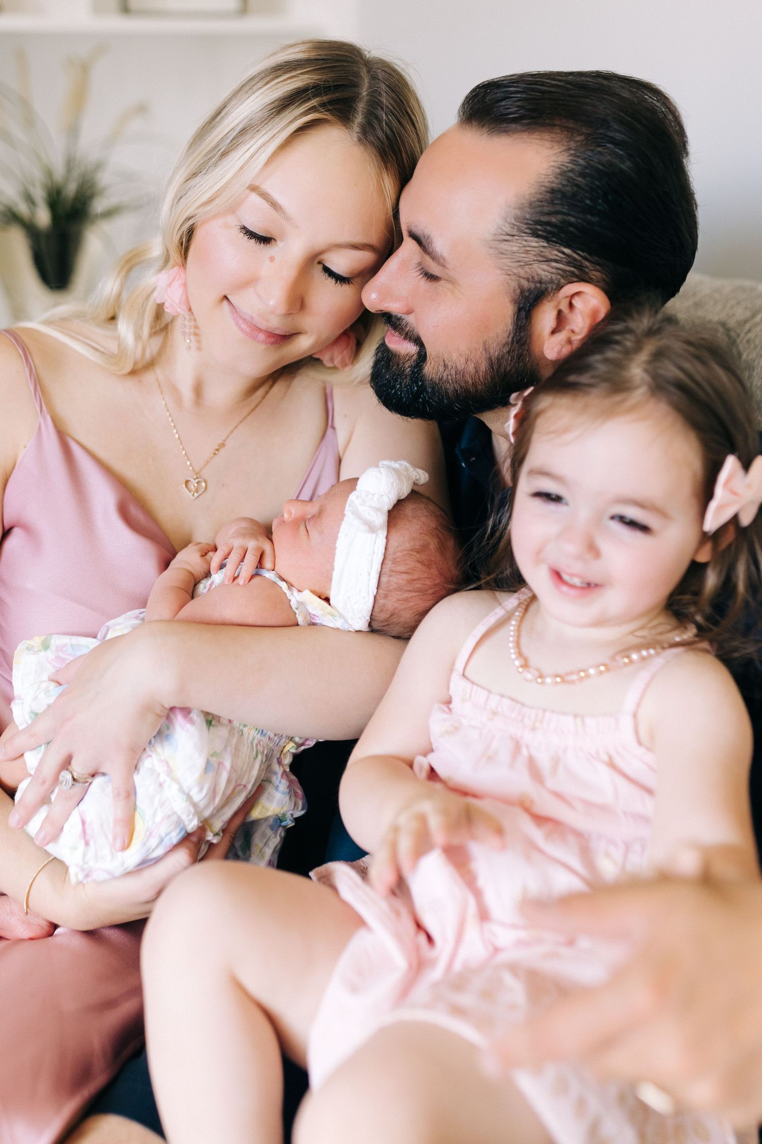 A family cuddles together on a couch in soft pink tones.